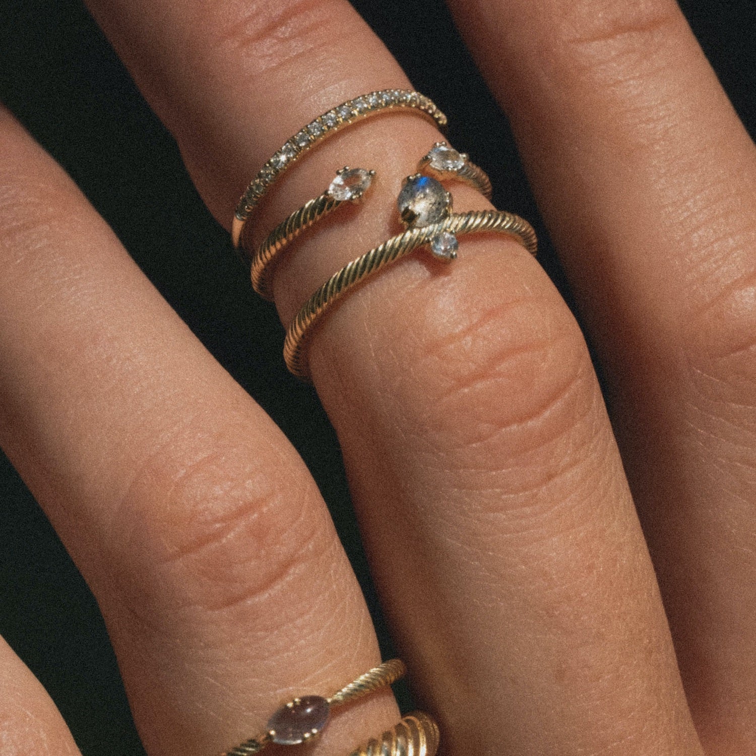 Close-up of curated ring stacks featuring textured gold and diamonds, labradorites, and white sapphires, worn on hand.