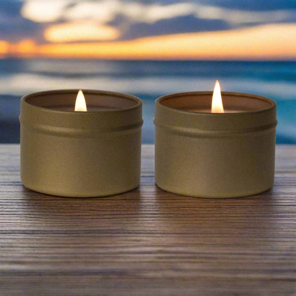 Coconut soy candles in gold tins, lit on a wooden table, against a serene tropical sky and beach shoreline in the background.