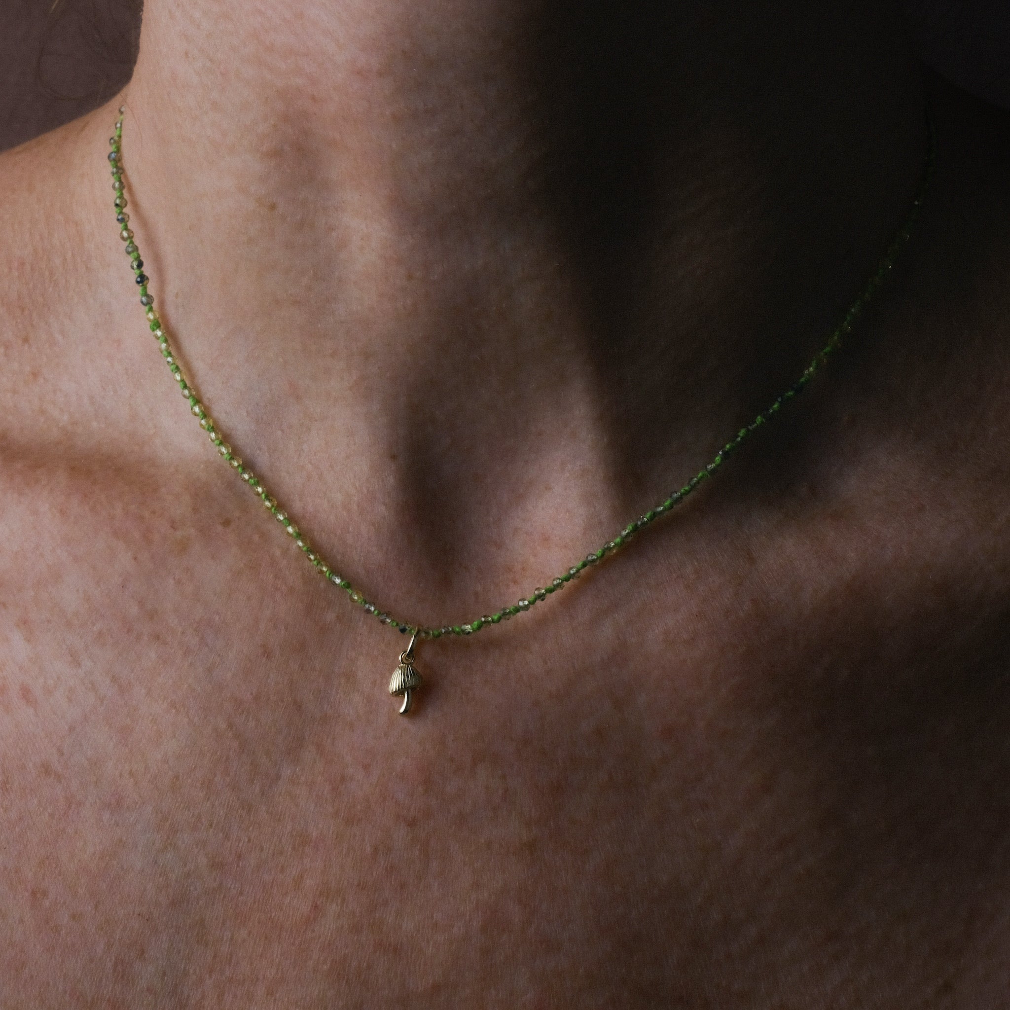 Knotted bead necklace with faceted tundra sapphire and bright green hemp, worn with tiny mushroom charm in solid gold.