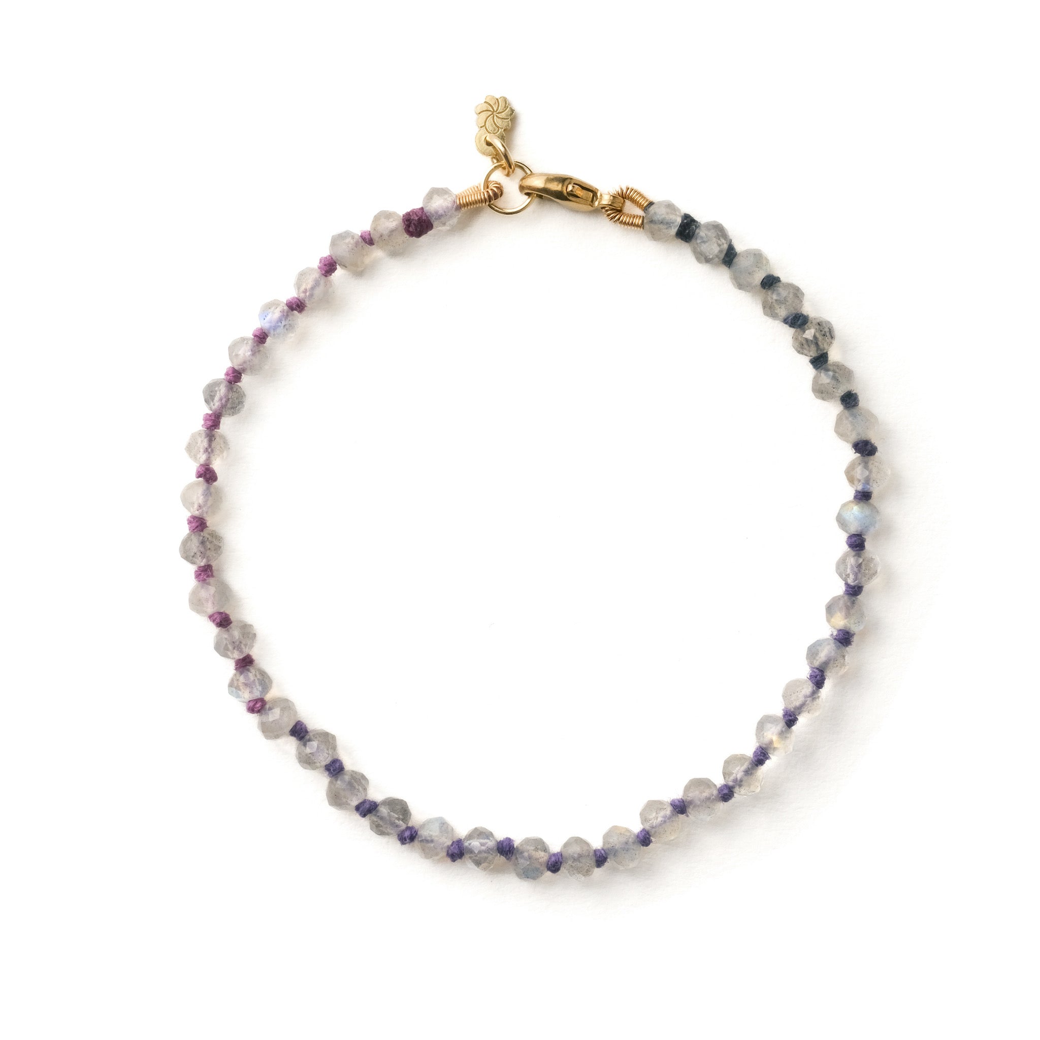 Knotted bead bracelet in faceted labradorite with blue-grey-violet ombré hemp and solid gold clasp, on white background.