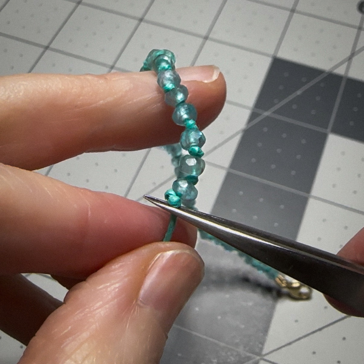 Close-up of faceted apatite gemstone beads being knotted with hemp cord.