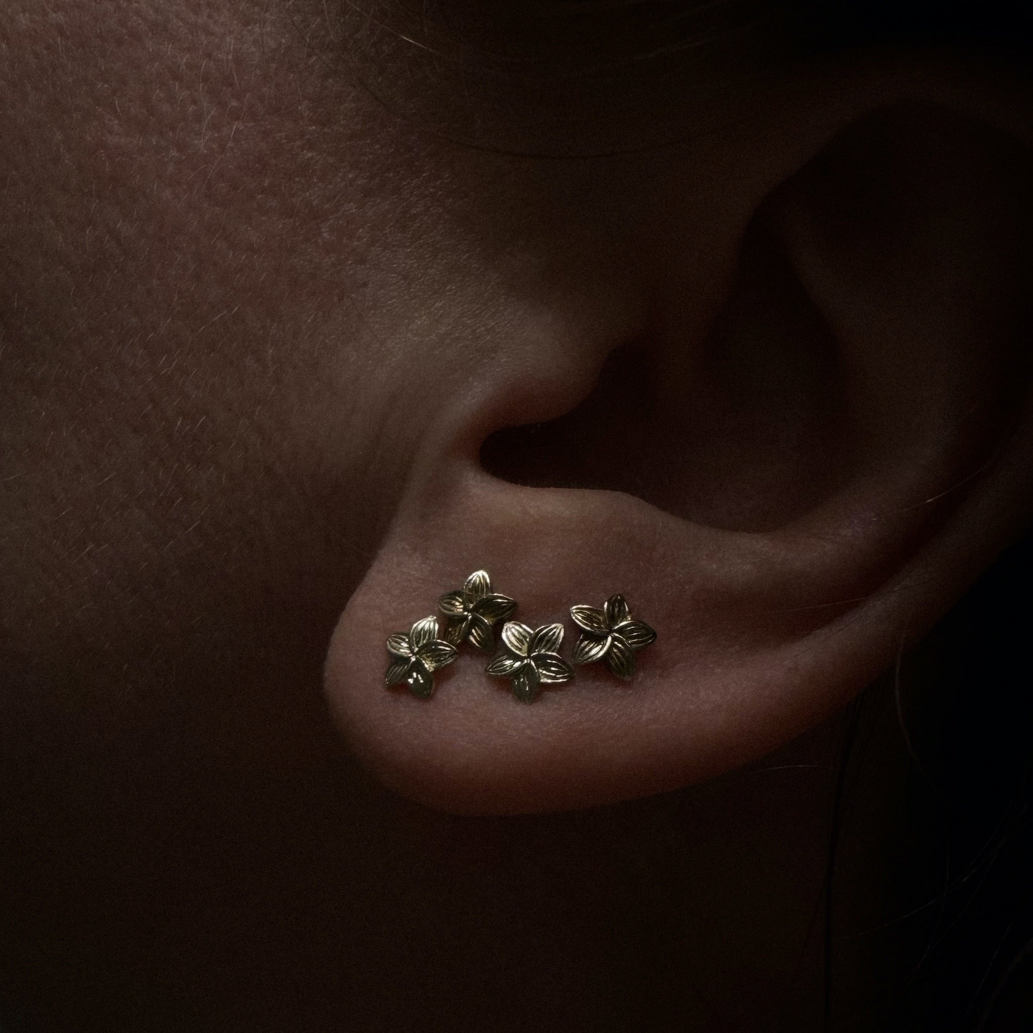 Solid gold tiny plumeria flower studs, with minimalist aesthetic, worn in cascading earring stack.