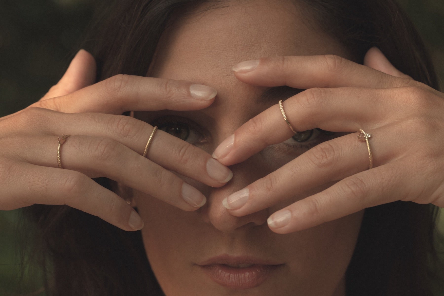 Woman with hands in front of eyes wearing solid gold rings with twisted texture and gemstones.