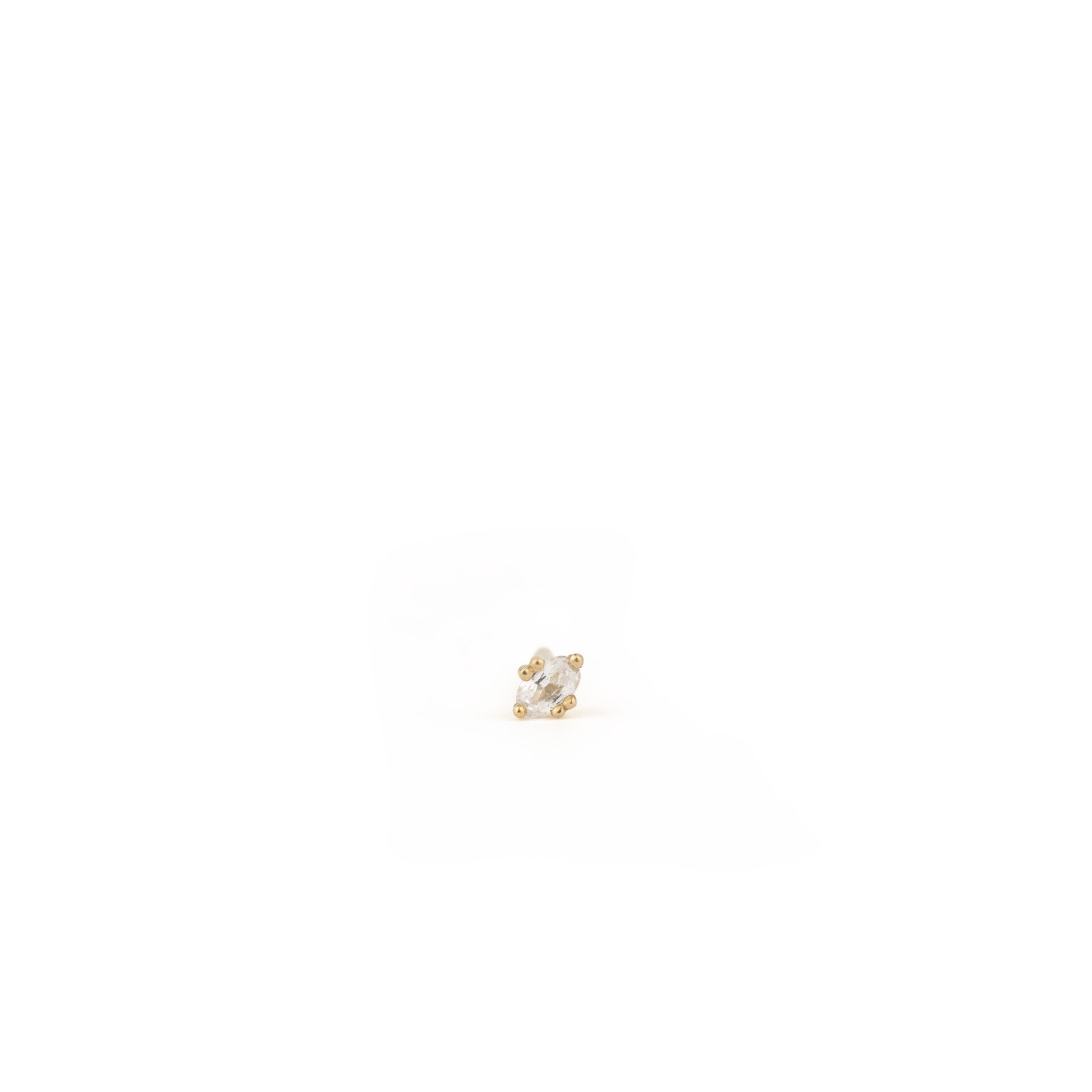 Tiny solid gold oval stud earring in white sapphire with minimalist design and unique prong setting, on white background.