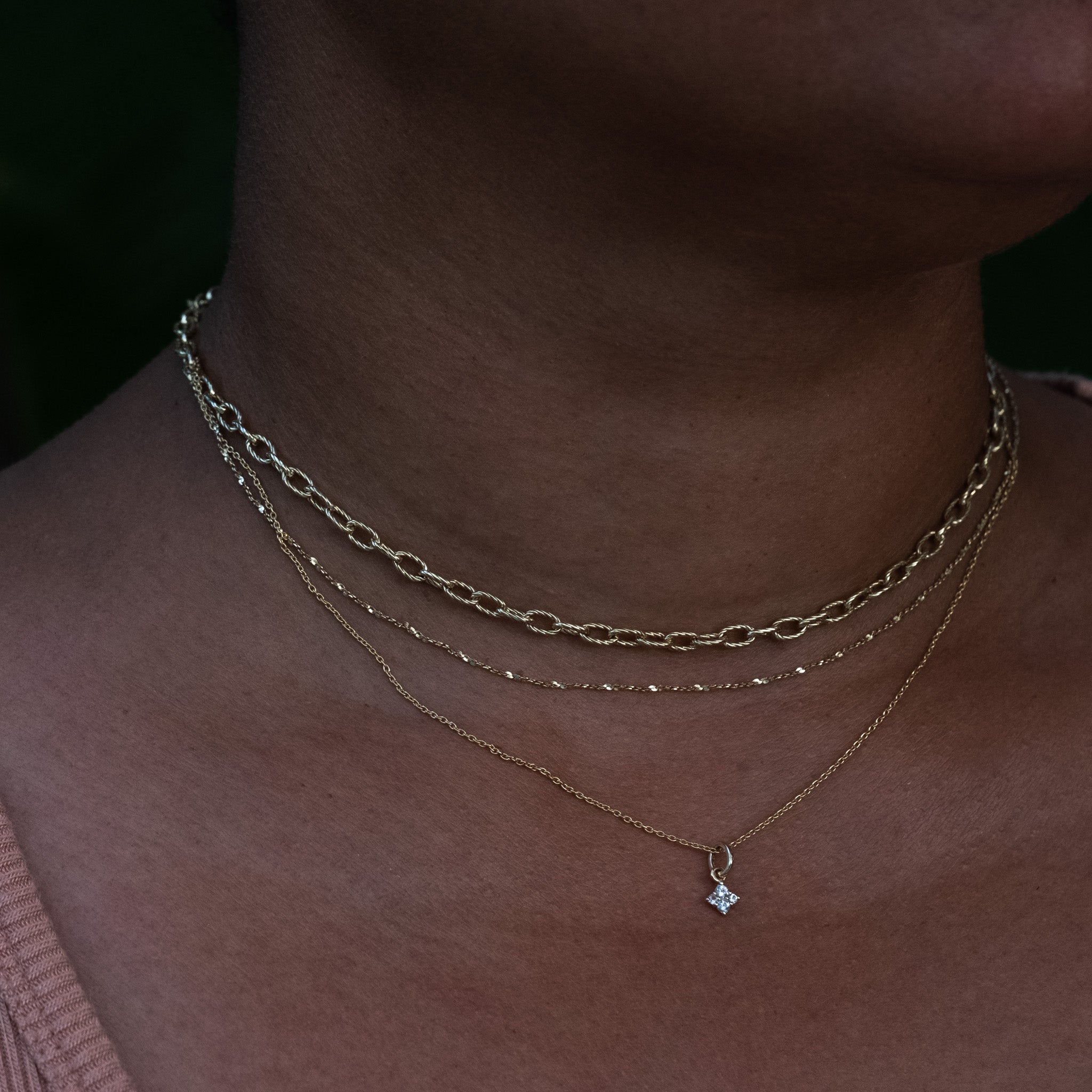 Solid gold cable and twisted serpentine chain necklaces styled with a white sapphire charm pendant, worn layered on neck.
