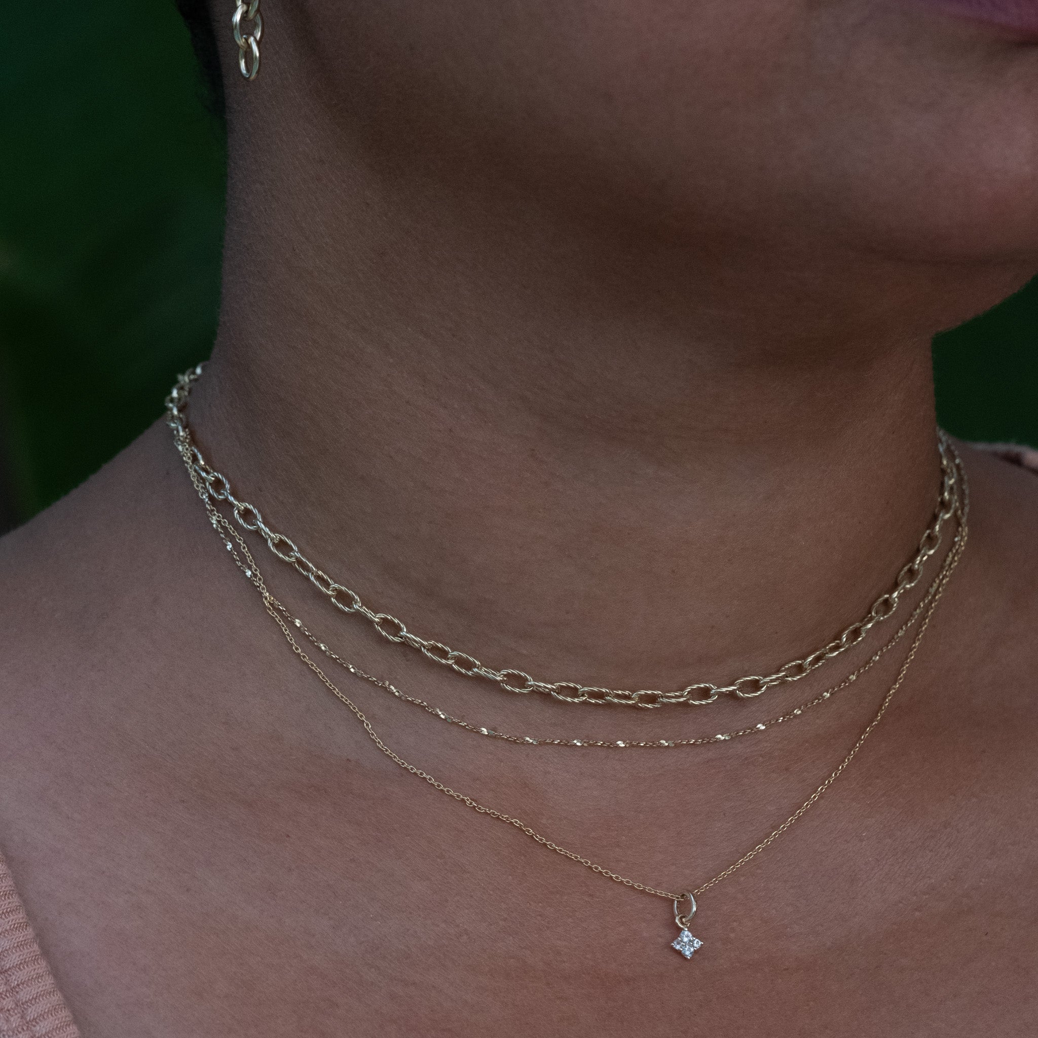 Solid gold cable and twisted serpentine chain necklaces styled with a white sapphire charm pendant, worn layered on neck.