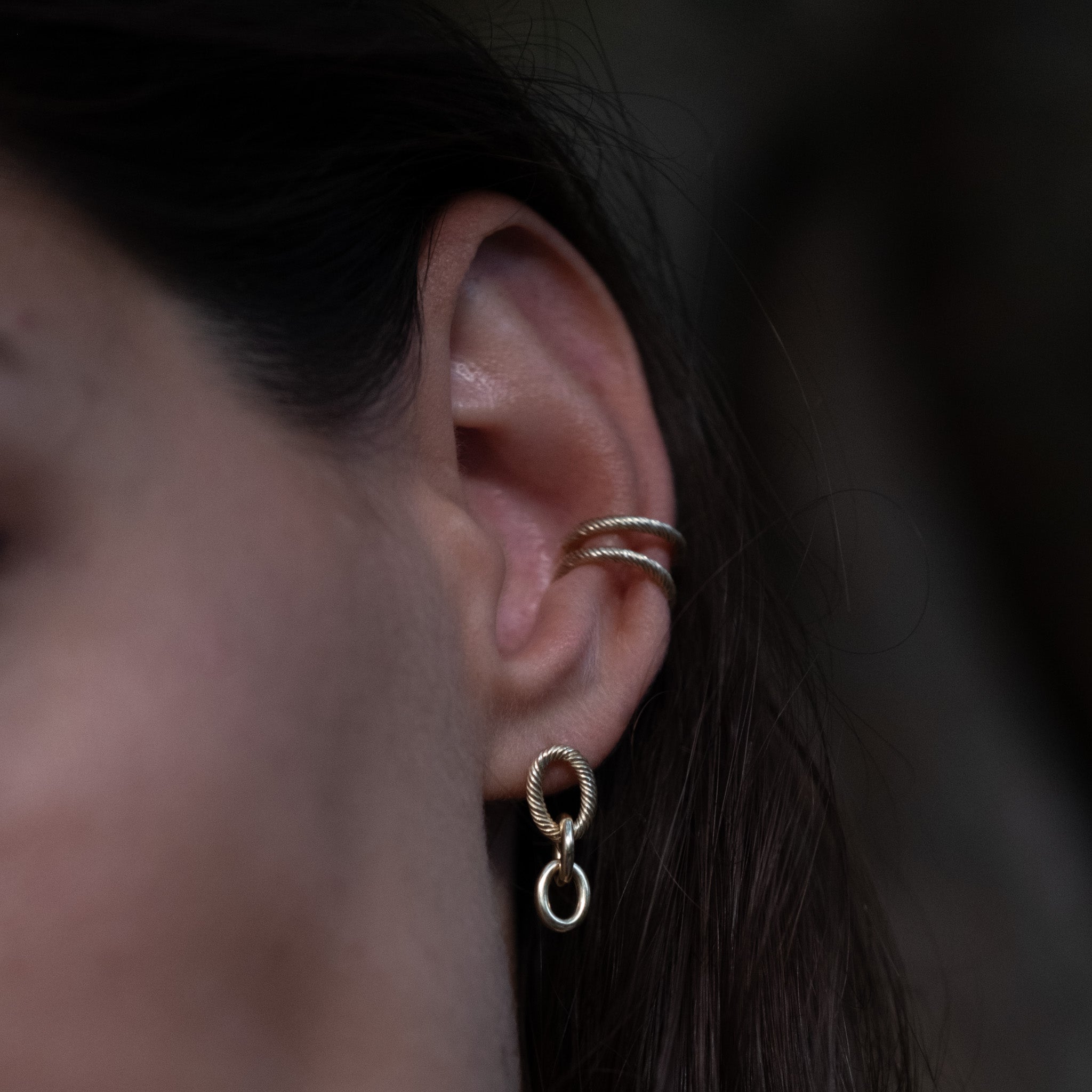 Two solid gold ear cuffs and oval cable chain link dangle earring with twisted texture, worn in a bold ear stack.