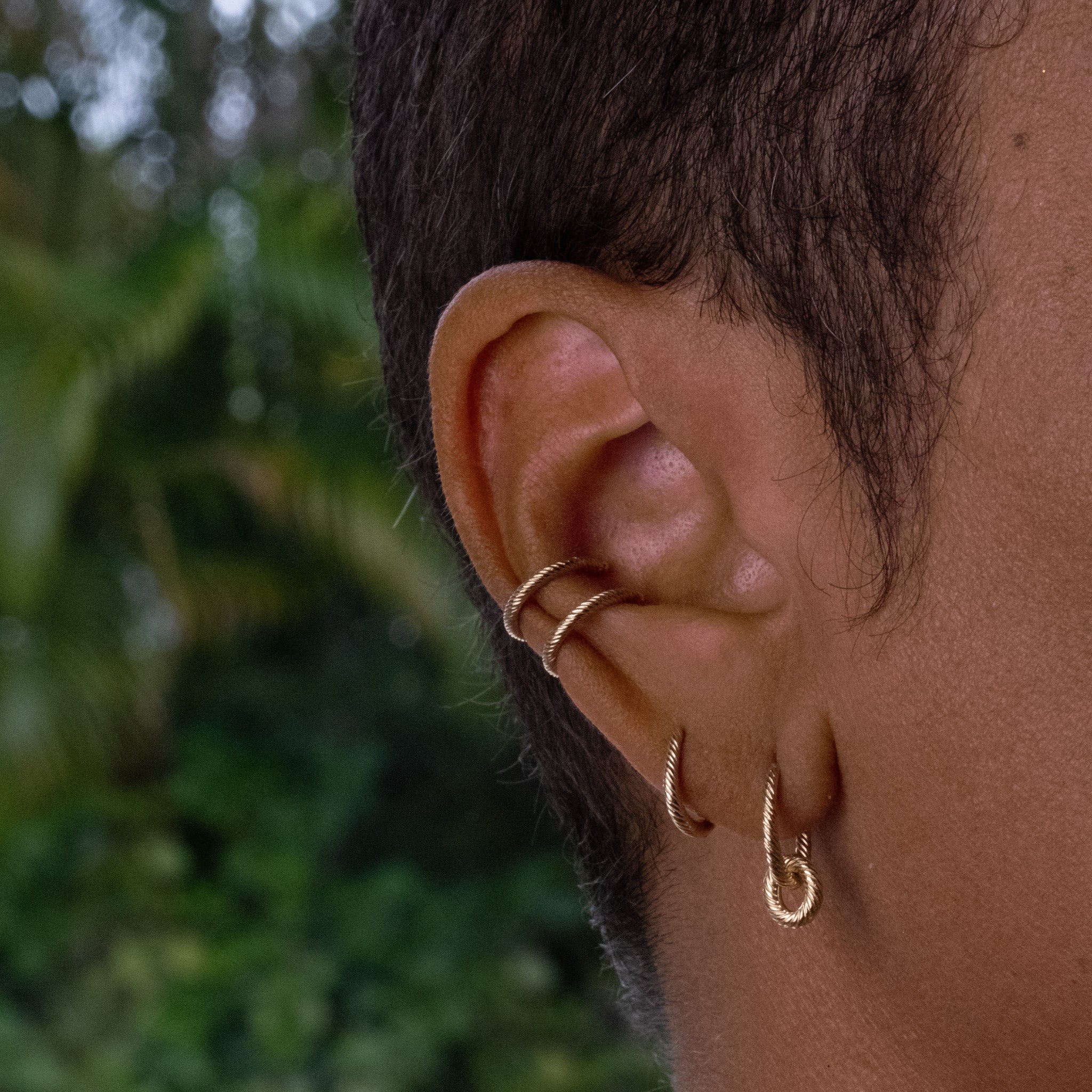 Solid gold hoop earring with link charm styled with huggie and two ear cuffs, worn in a bold textured ear stack.