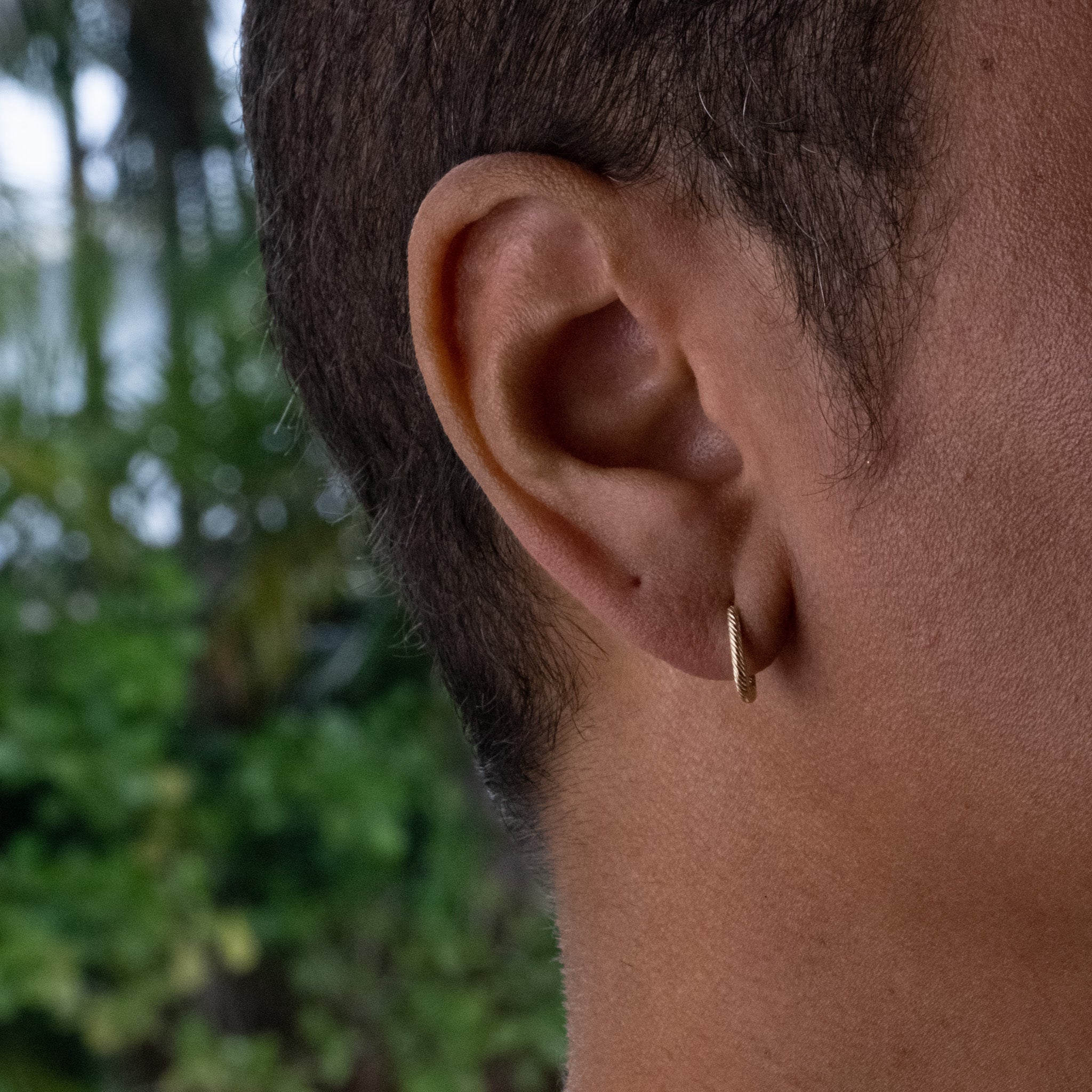 Solid gold huggie hoop earring with twisted texture and minimalist design, worn on ear.