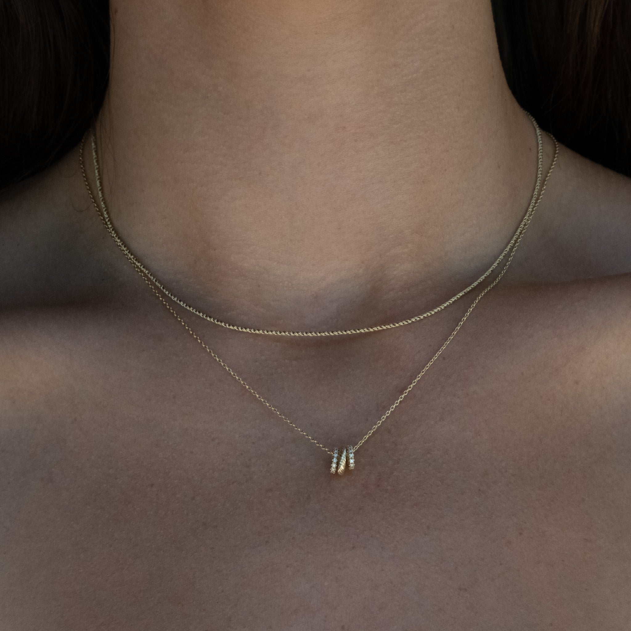 Solid gold rope chain layered on neck with necklace featuring diamond and textured gold link charms.