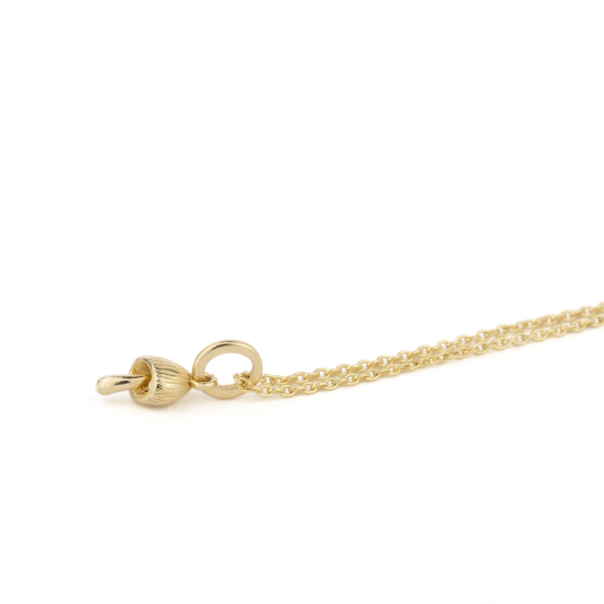 Solid gold necklace with tiny mushroom charm pendant and cable chain, shown laying angled on white background.