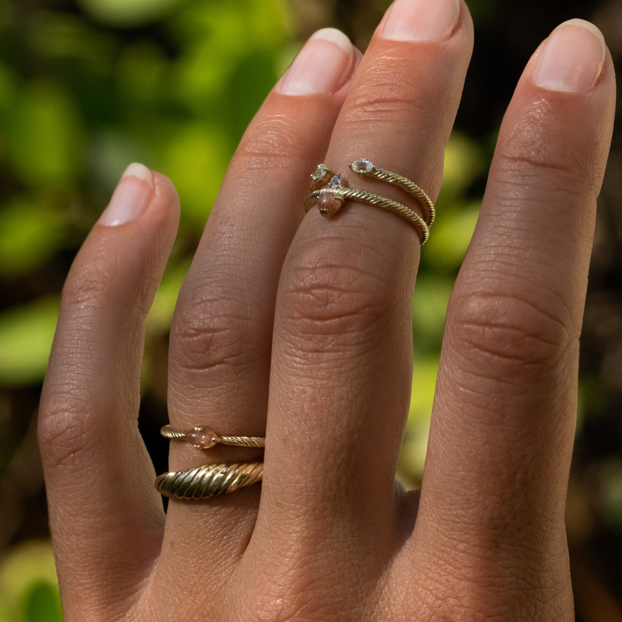 Solid gold rings stacked on hand, with twisted texture, sunstone, white sapphire, and minimalist aesthetic.