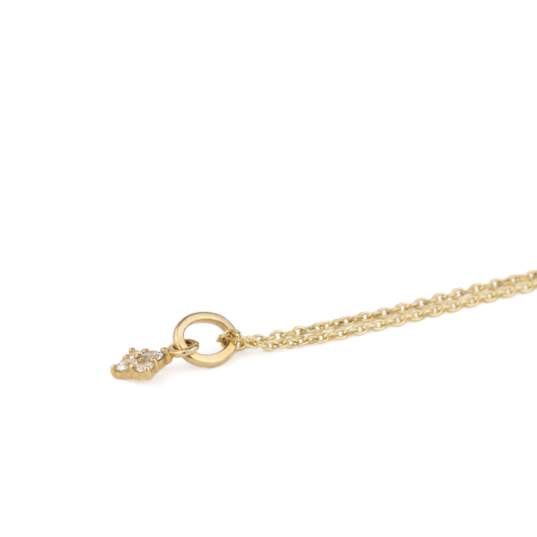 Tiny solid gold white sapphire pendant in minimalist celestial design on chain, shown laying angled on white background.