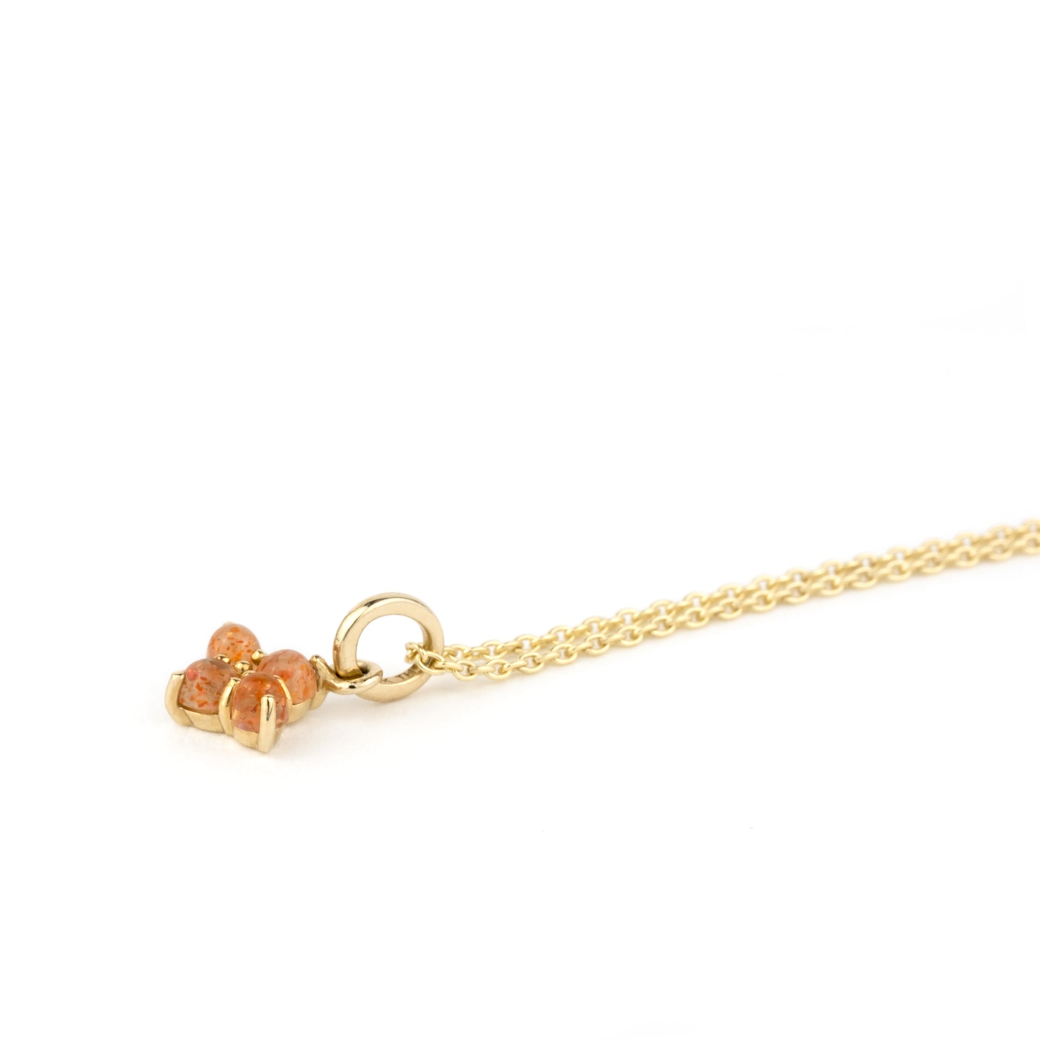 Solid gold charm pendant with cabochon sunstones, in a minimalist design, on cable chain, laying angled on white background.