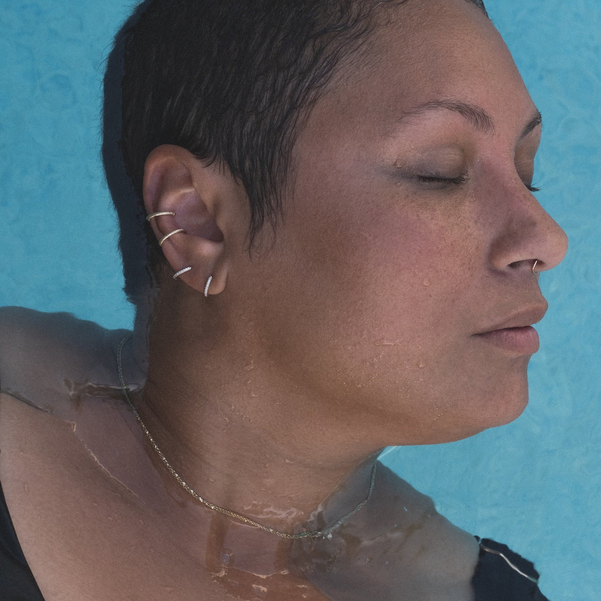 Model in water wearing diamond hoop earrings and textured yellow gold ear cuffs.