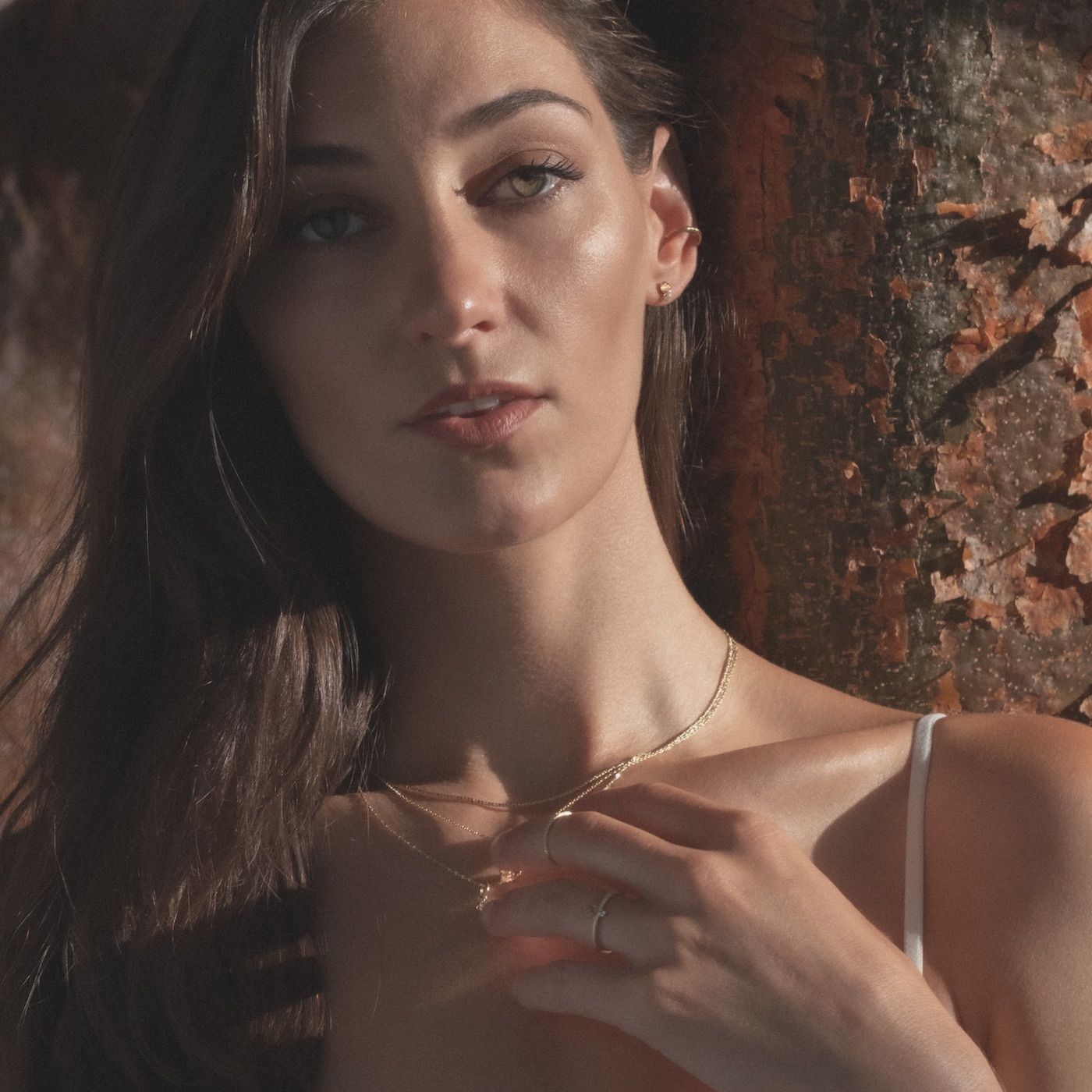 Model wearing yellow gold and gemstone Aiden Jae jewelry next to tree.