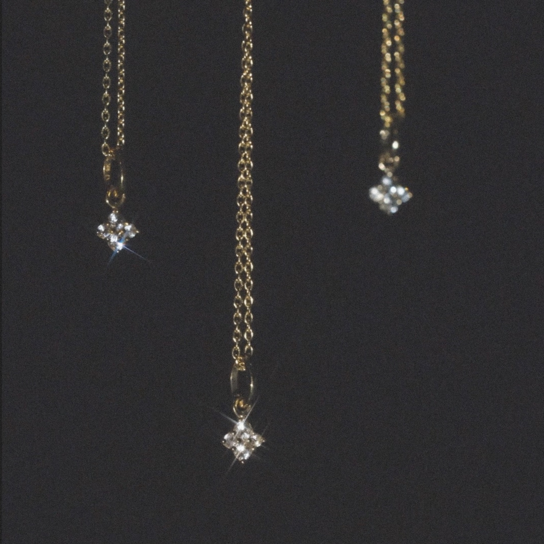Aiden Jae's Stardust Charm Necklaces in yellow gold and white sapphire with cable chain hanging and sparkling in front on dark background.