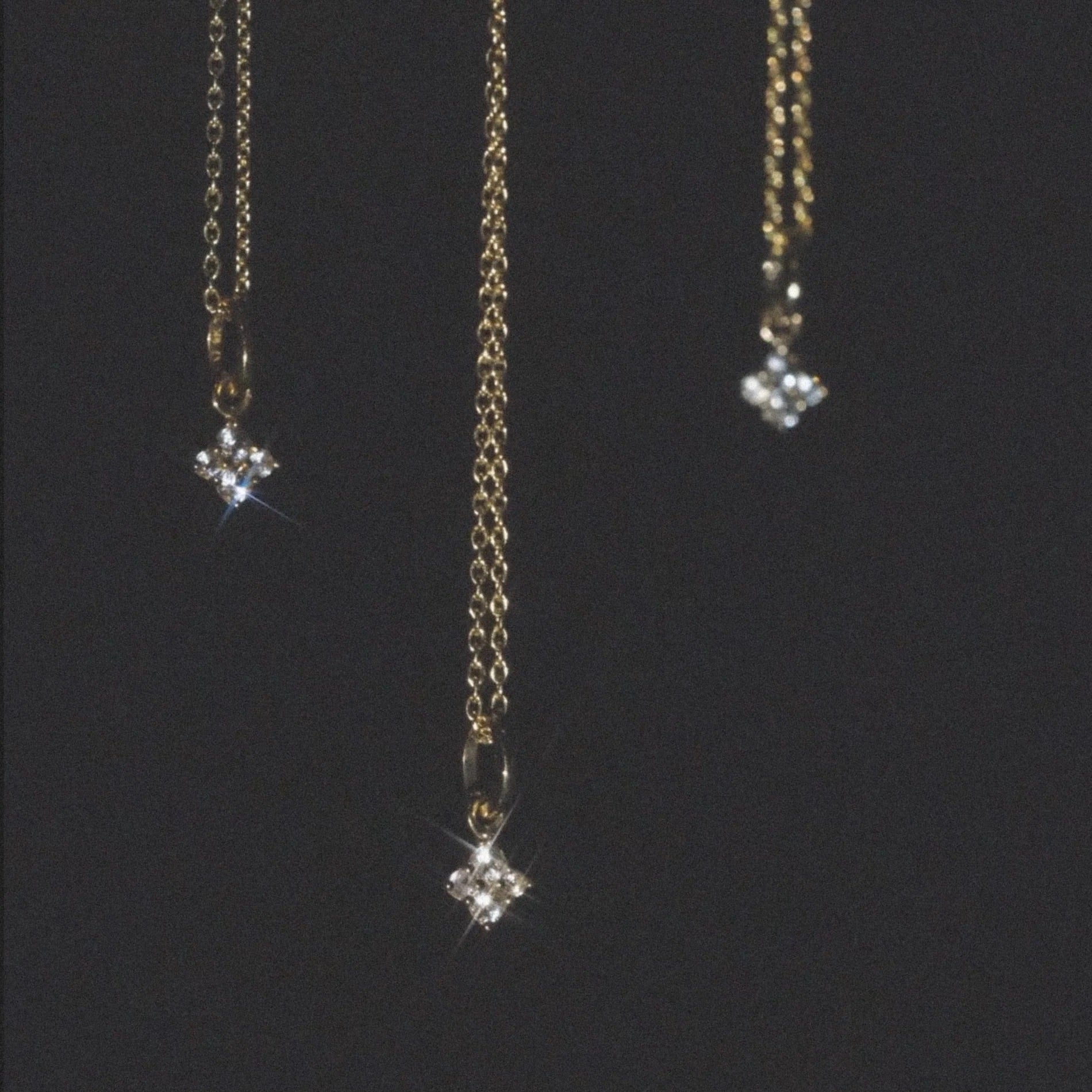 Solid gold minimalist charm pendants with white sapphires on cable chains, celestial design against dark background.