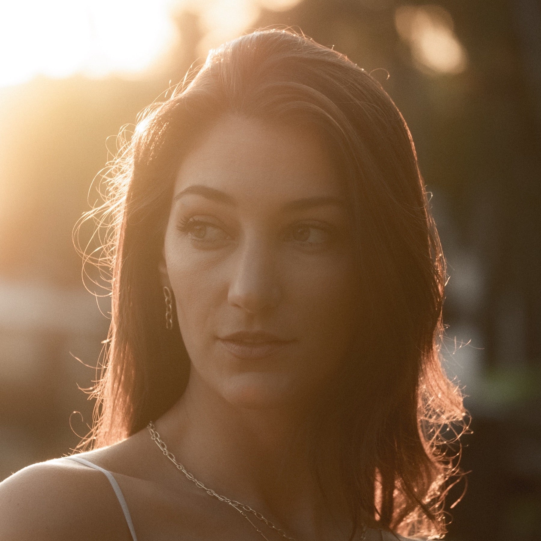 Model wearing textured yellow gold link earrings and chains with light from sunrise shining on her from behind.