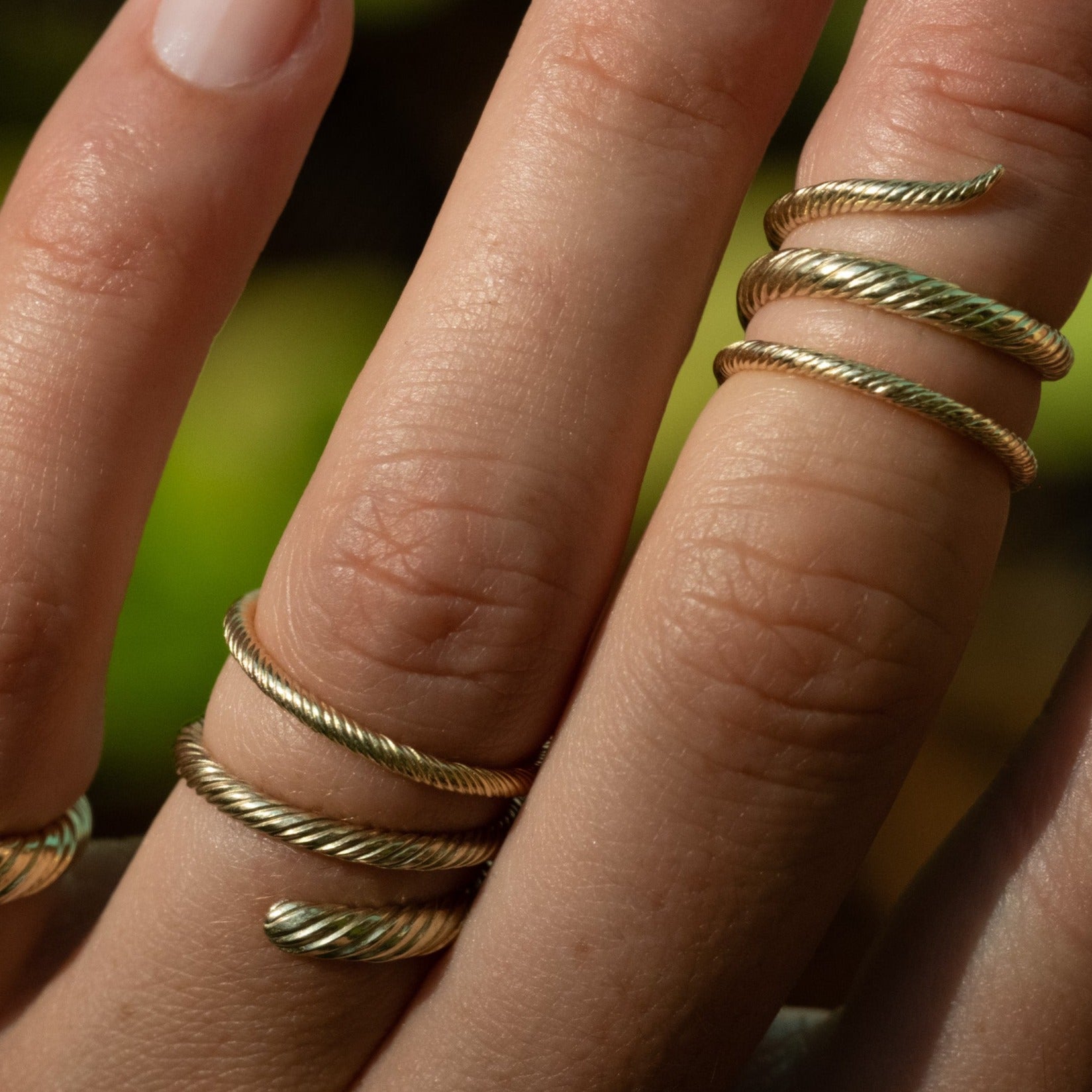 Close-up of coiled wrap rings and thin band rings in solid gold with twisted texture, worn stacked on hand.