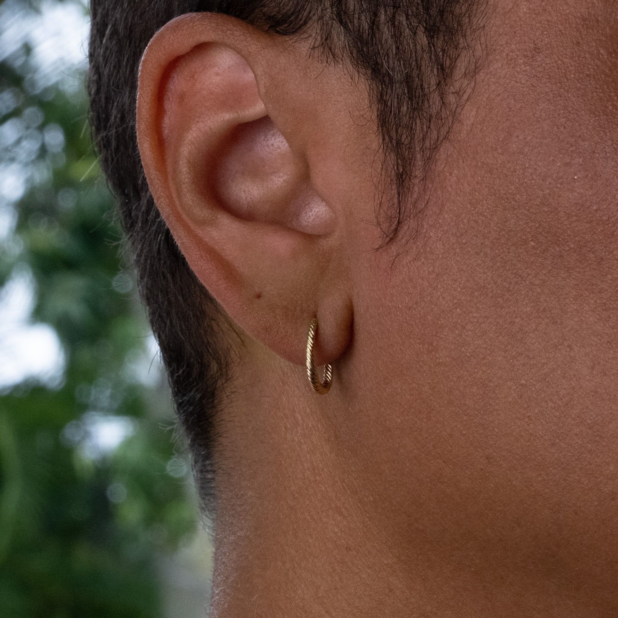 Solid gold oval hoop earring with twisted texture and minimalist design, worn on ear.