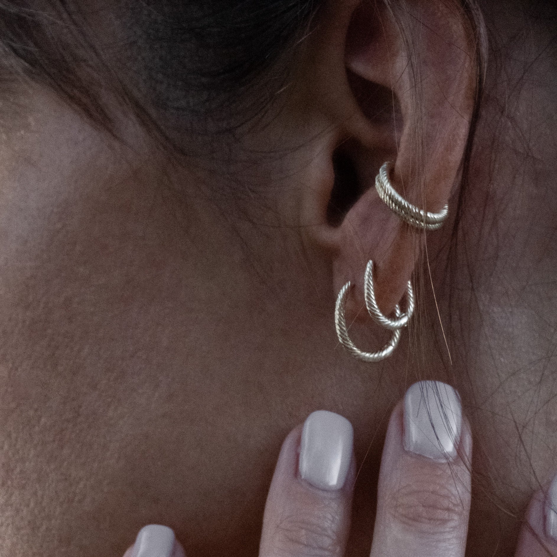 Solid gold hoop and huggie earrings styled with doubled ear cuffs featuring twisted texture, worn in a minimalist ear stack.