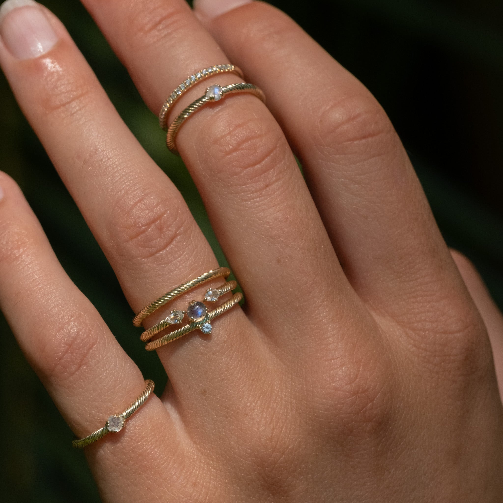 Solid gold ring stacks with twisted texture in labradorite, white sapphire, rainbow moonstone, diamond, worn on hand.