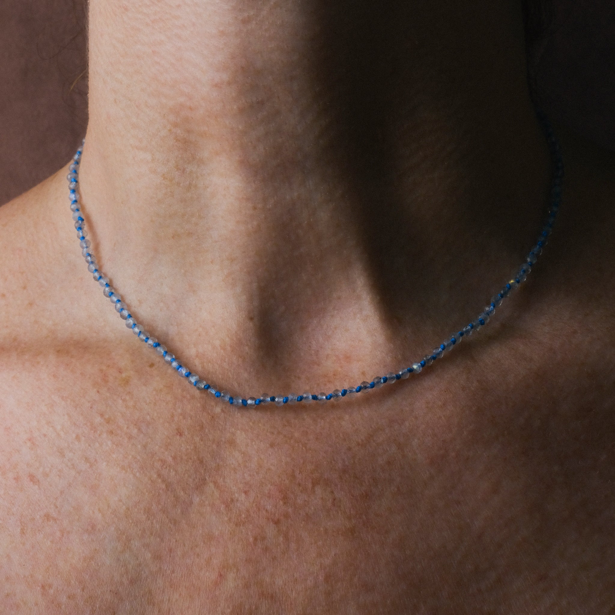 Hand-Knotted Aurora Necklace worn on neck, featuring faceted labradorite beads, bright blue hemp, and solid 9k gold.