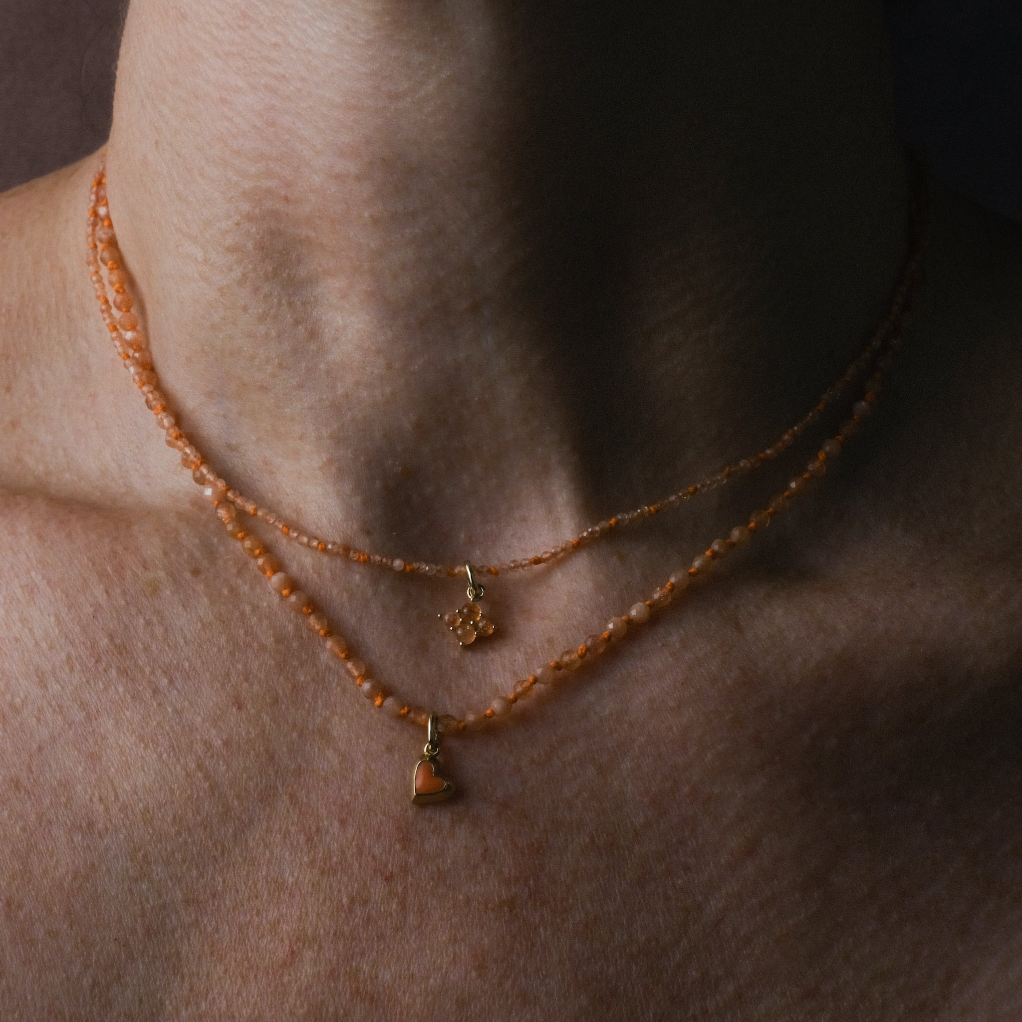 Hand-Knotted Sunshower Necklace with Sunrise Charm worn on neck, featuring faceted sunstone beads, bright orange hemp, and solid 9k gold. Layered with First Blush Necklace and Mini Heart Charm.