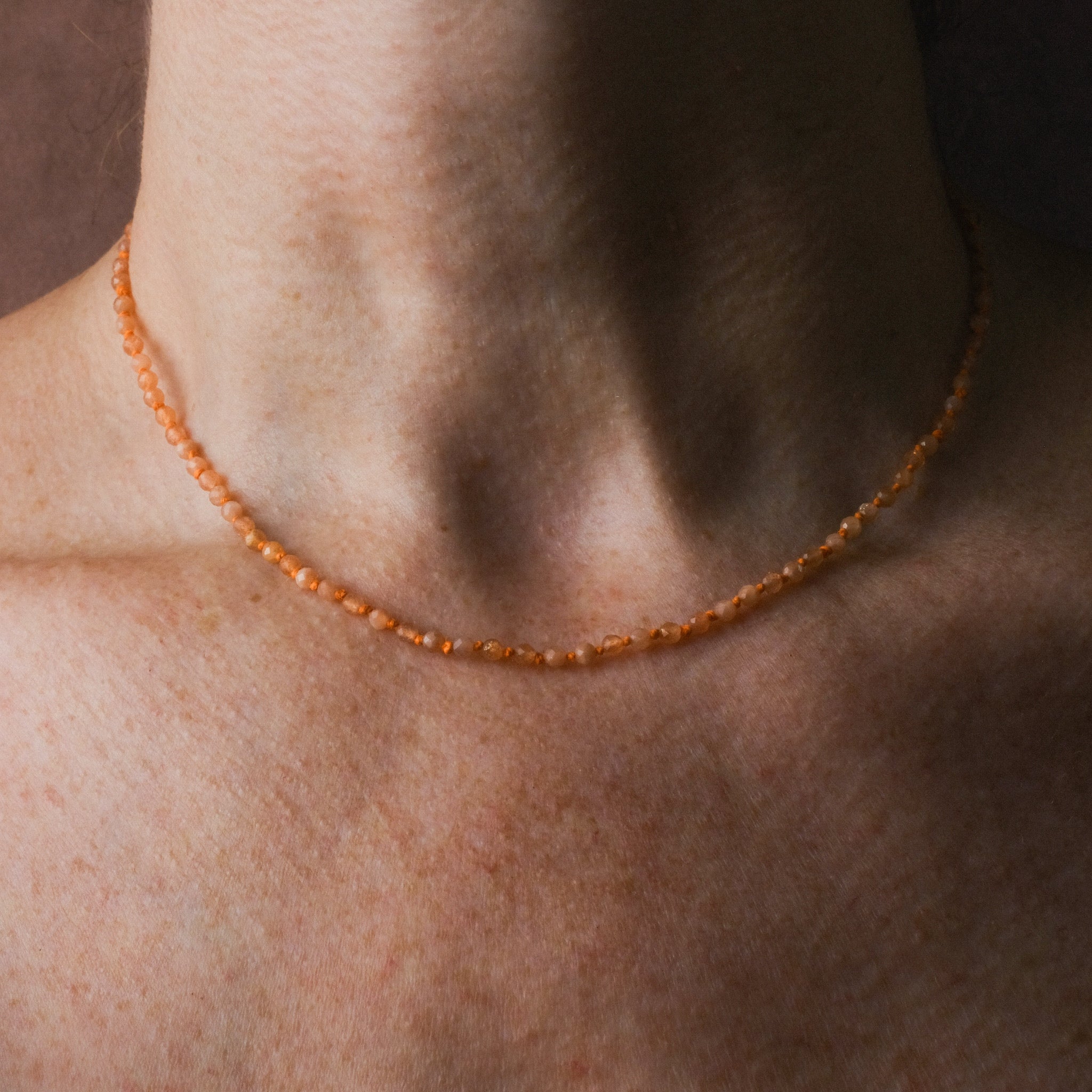 Knotted bead necklace with faceted sunstone and bright orange hemp, worn on neck.