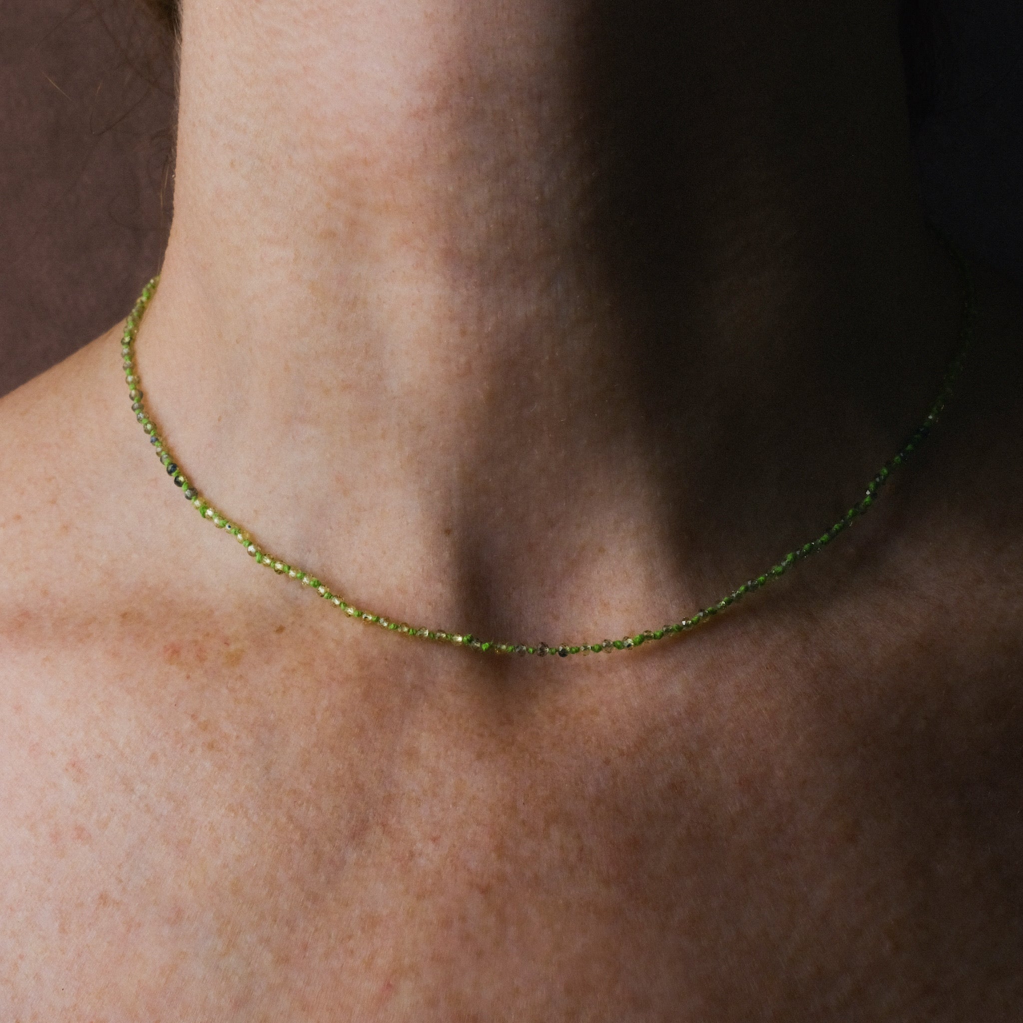 Knotted bead necklace with faceted tundra sapphire and bright green hemp, worn on neck.