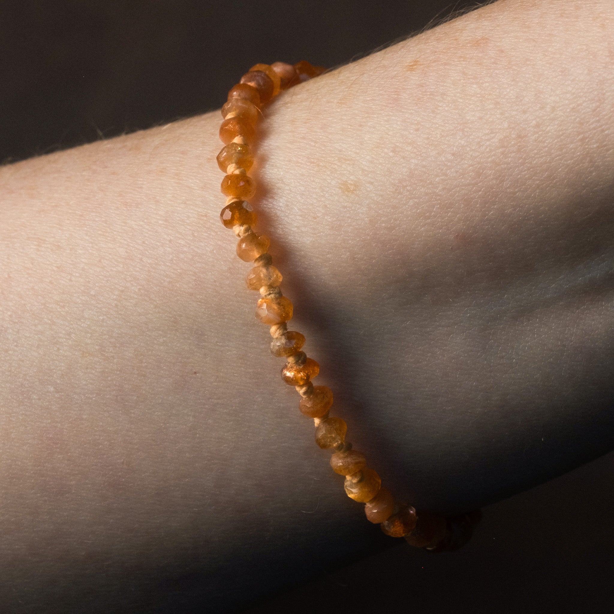 Knotted bead bracelet with faceted sunstone and ombré hemp in warm sunset hues, worn on wrist.