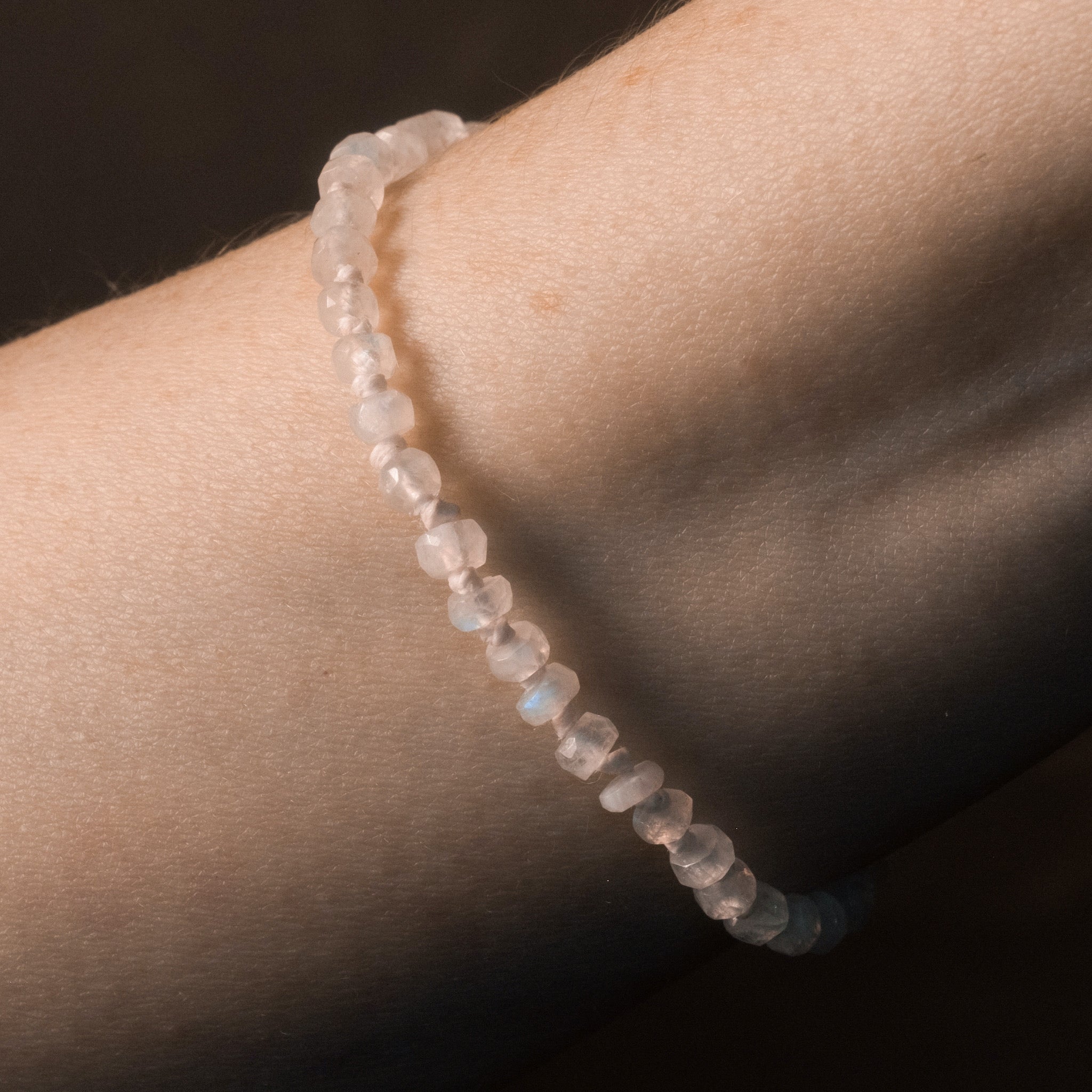 Knotted bead bracelet with faceted rainbow moonstone and white hemp, worn on wrist.