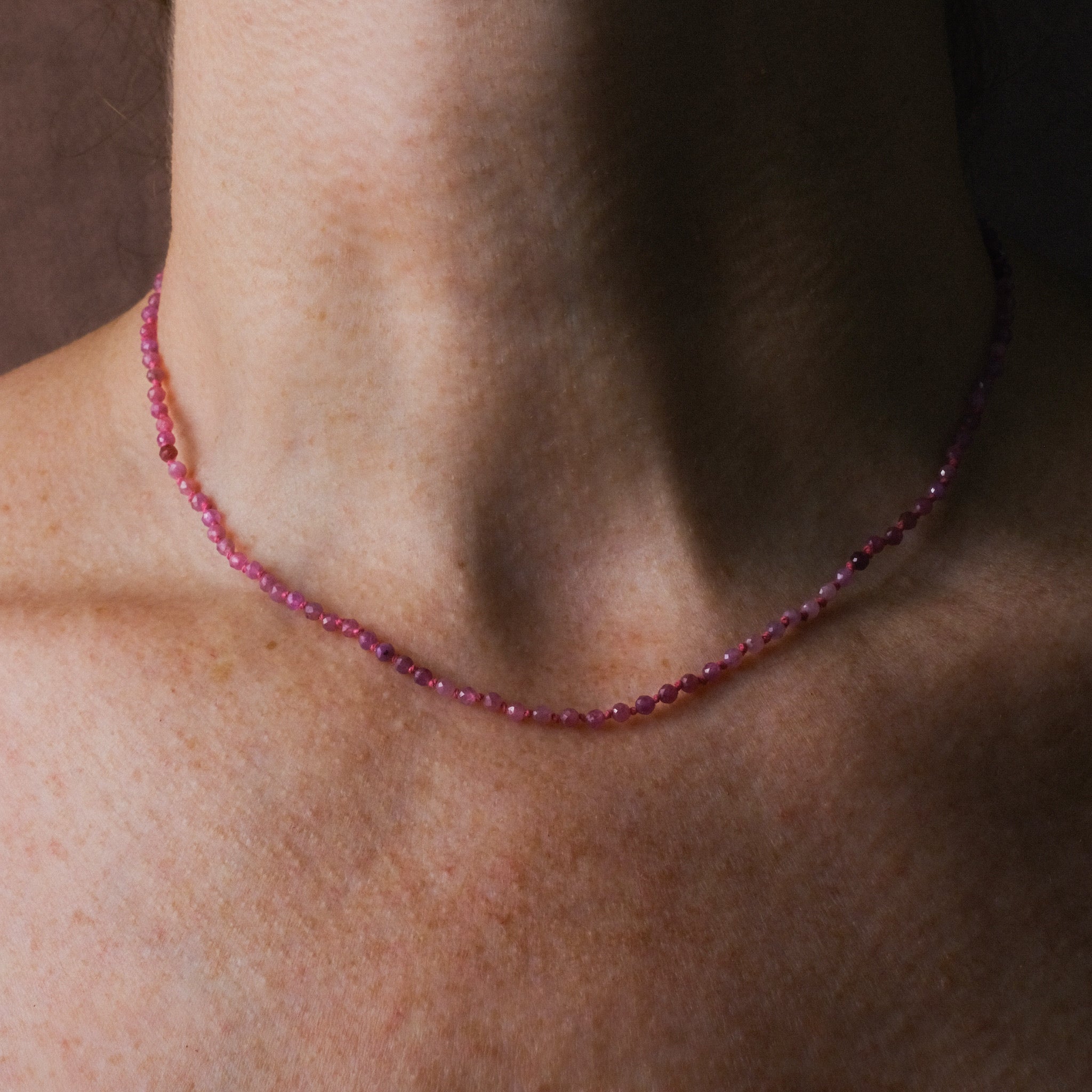 Knotted bead necklace with faceted shaded pink sapphire and bright pink hemp, worn on neck.