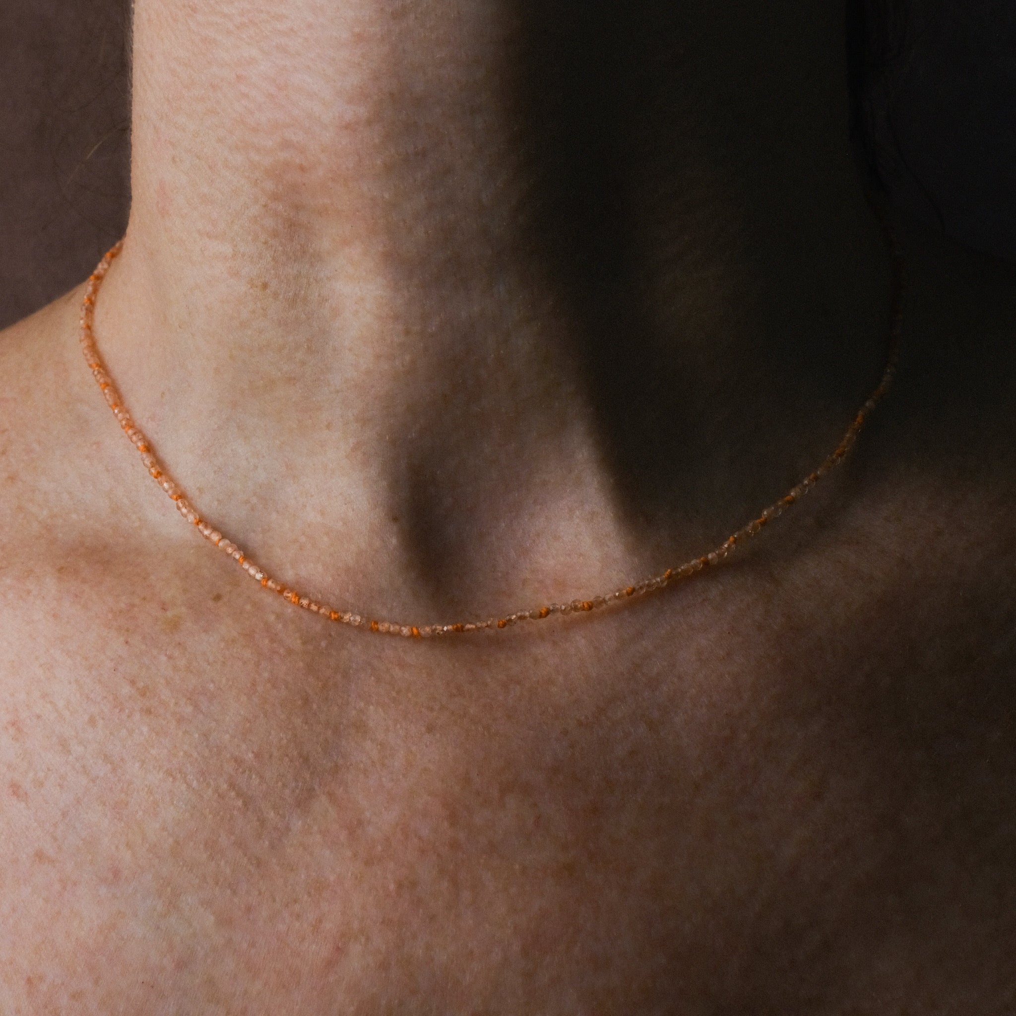 Knotted bead necklace with faceted sunstone and bright orange hemp, worn on neck.