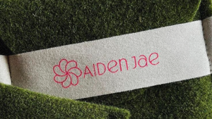 Closeup of Aiden Jae green felt pouch and cream cotton band with hot pink logo.