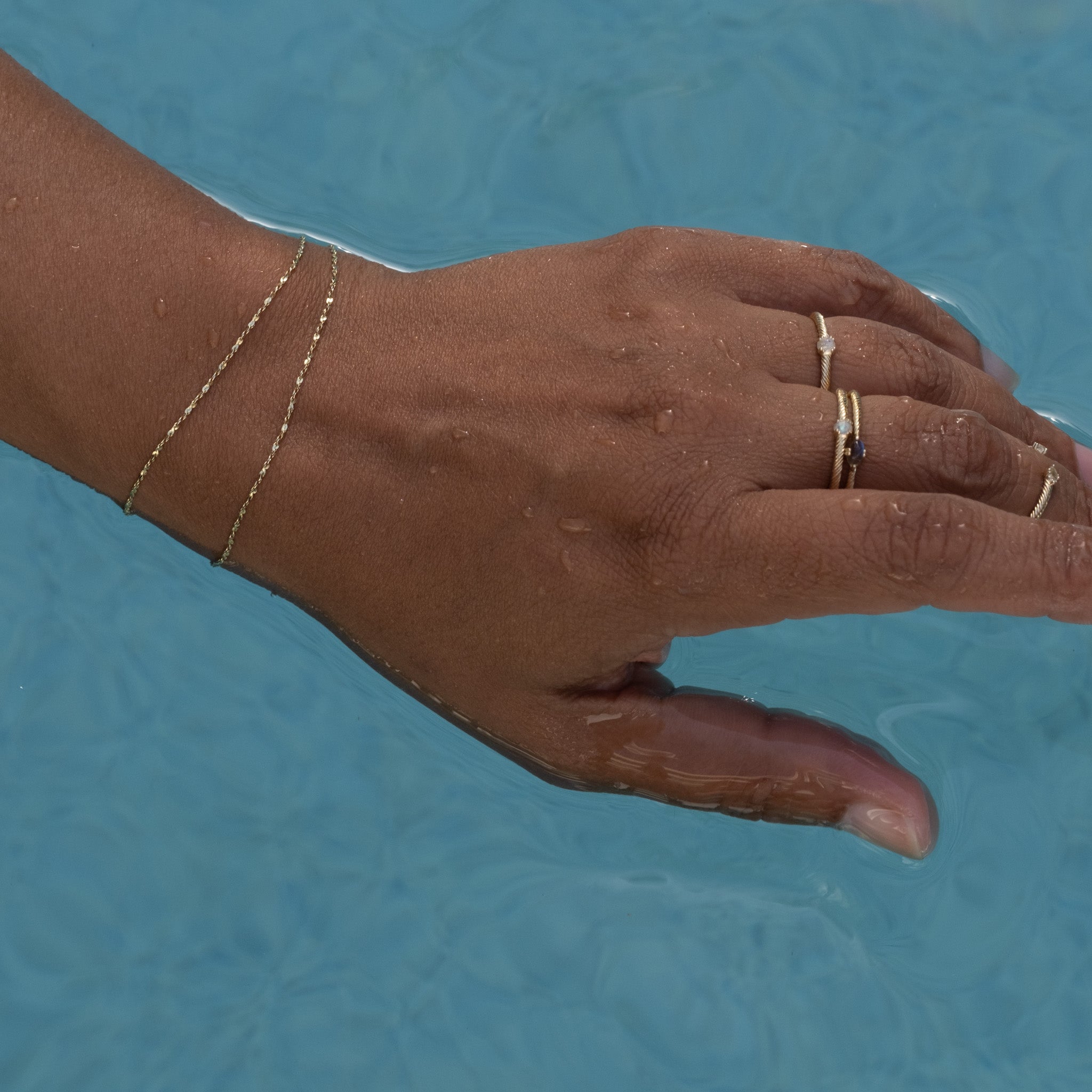 A person's hand holding an Aiden Jae Starshine Chain Bracelet in the water.