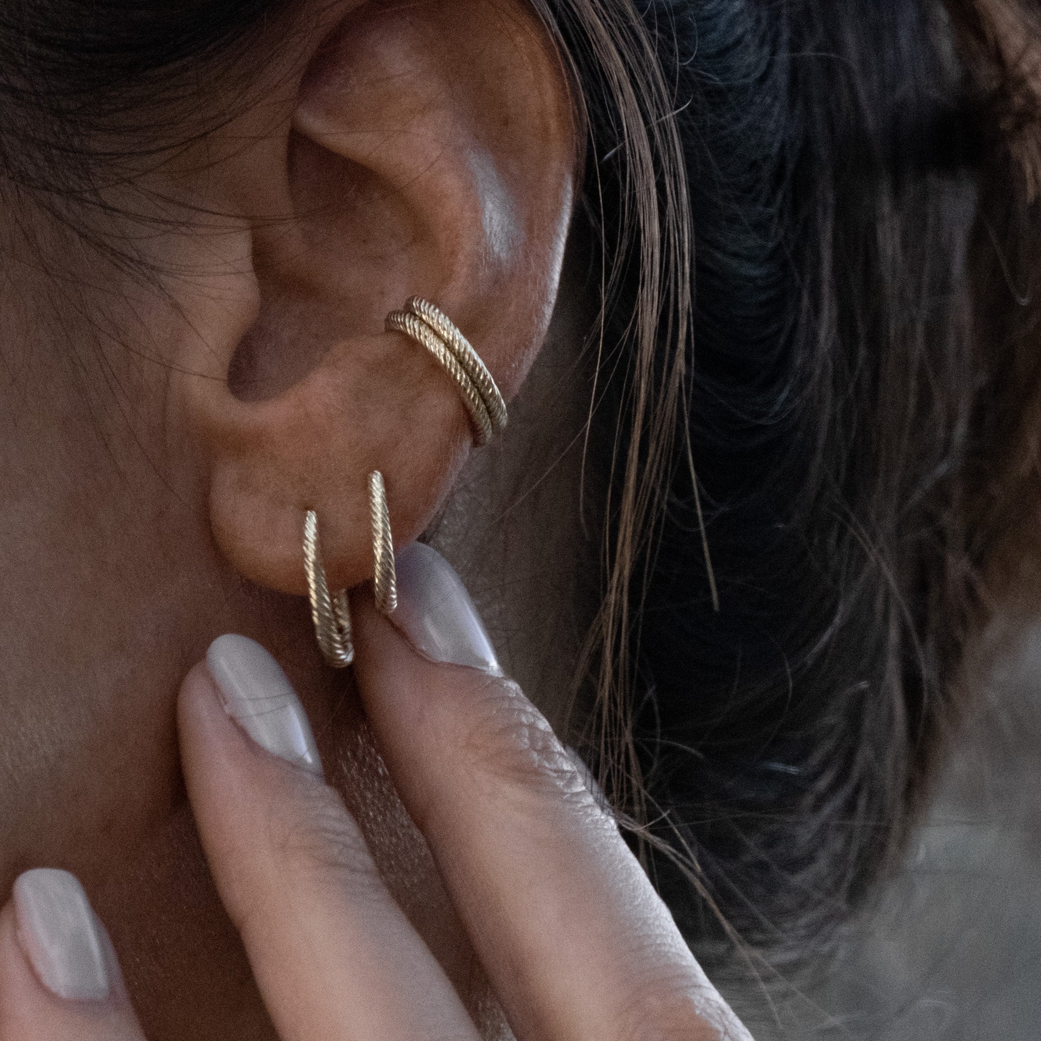 A close up of a person wearing a pair of Aiden Jae Banyan Huggie earrings.