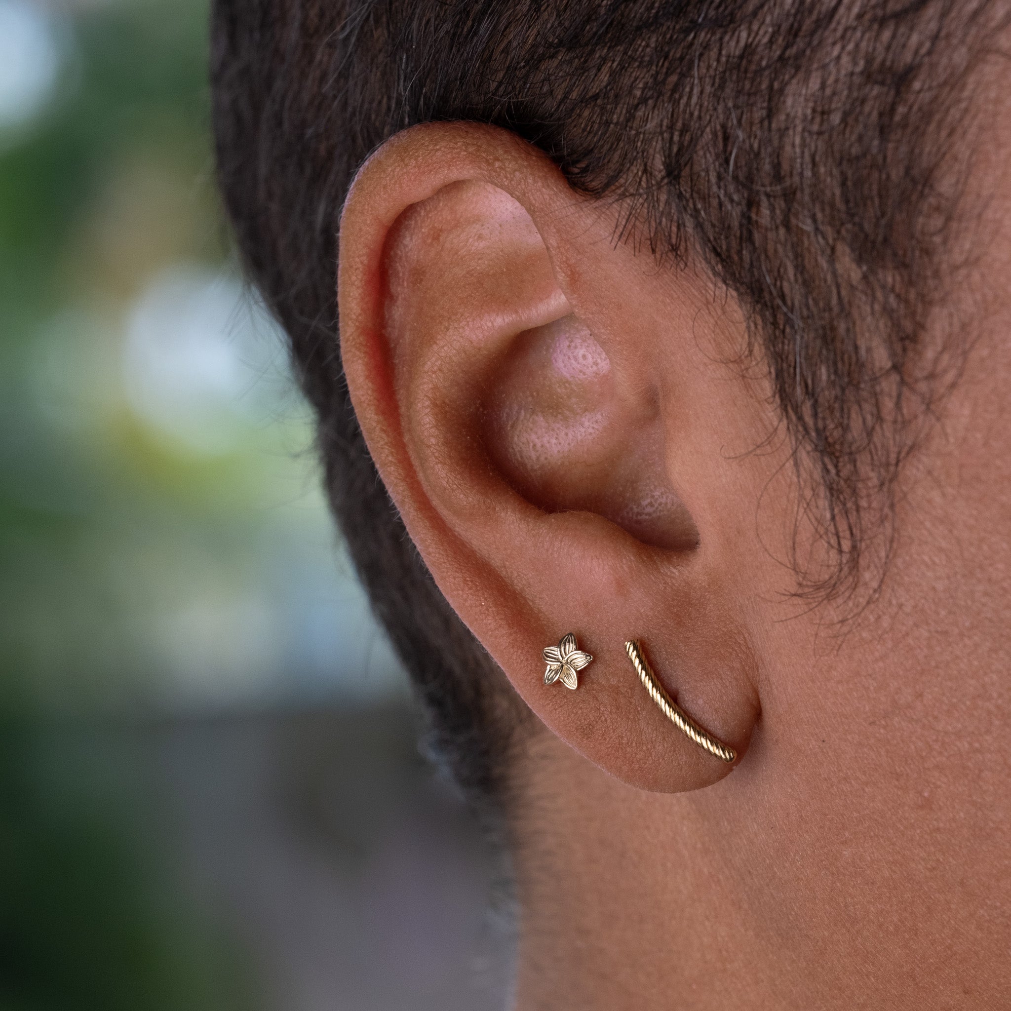 A close up of a person's ear wearing Aiden Jae's Mini Plumeria Studs.