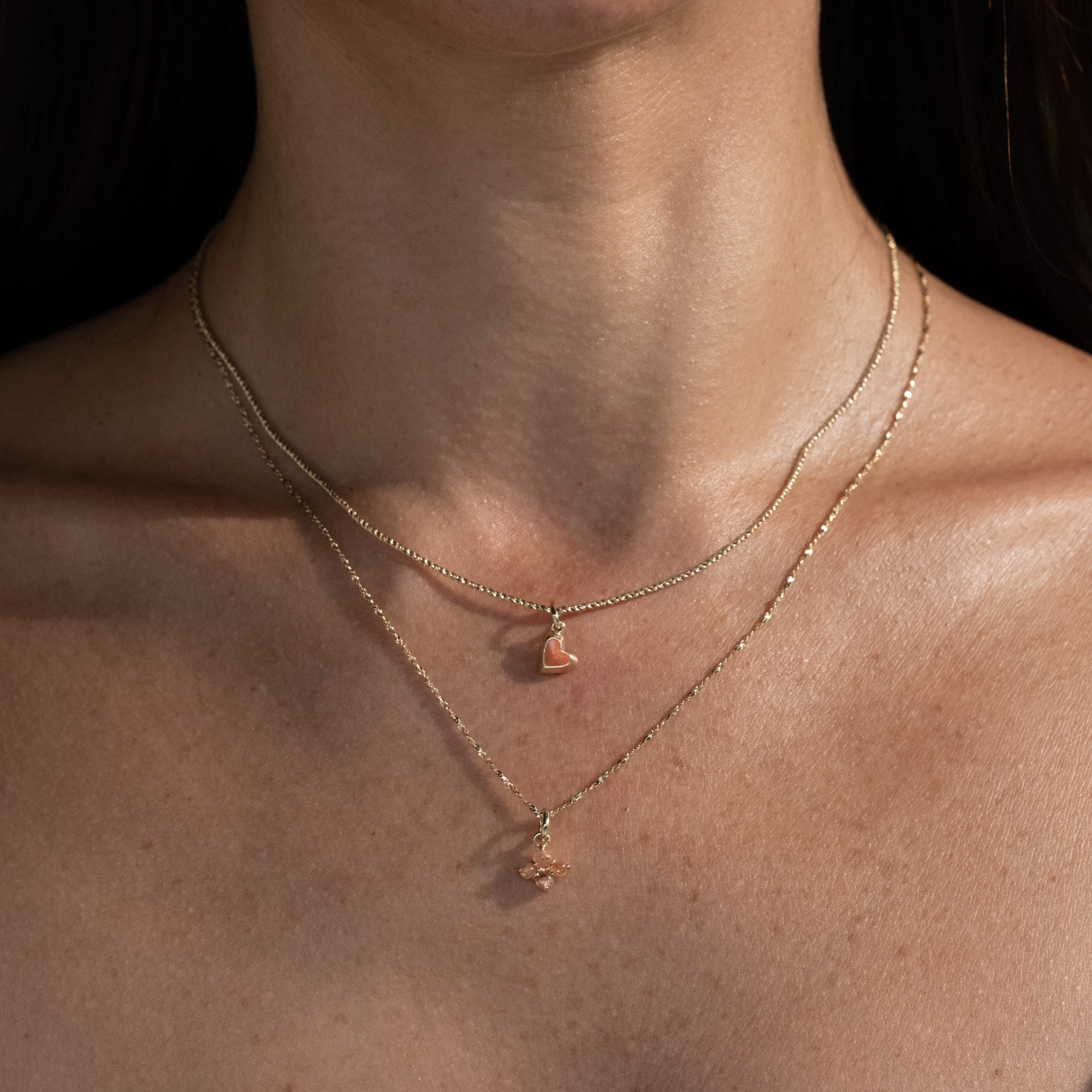 Solid gold rope chain with coral enamel heart charm and twisted serpentine chain with sunstone charm worn layered on neck.