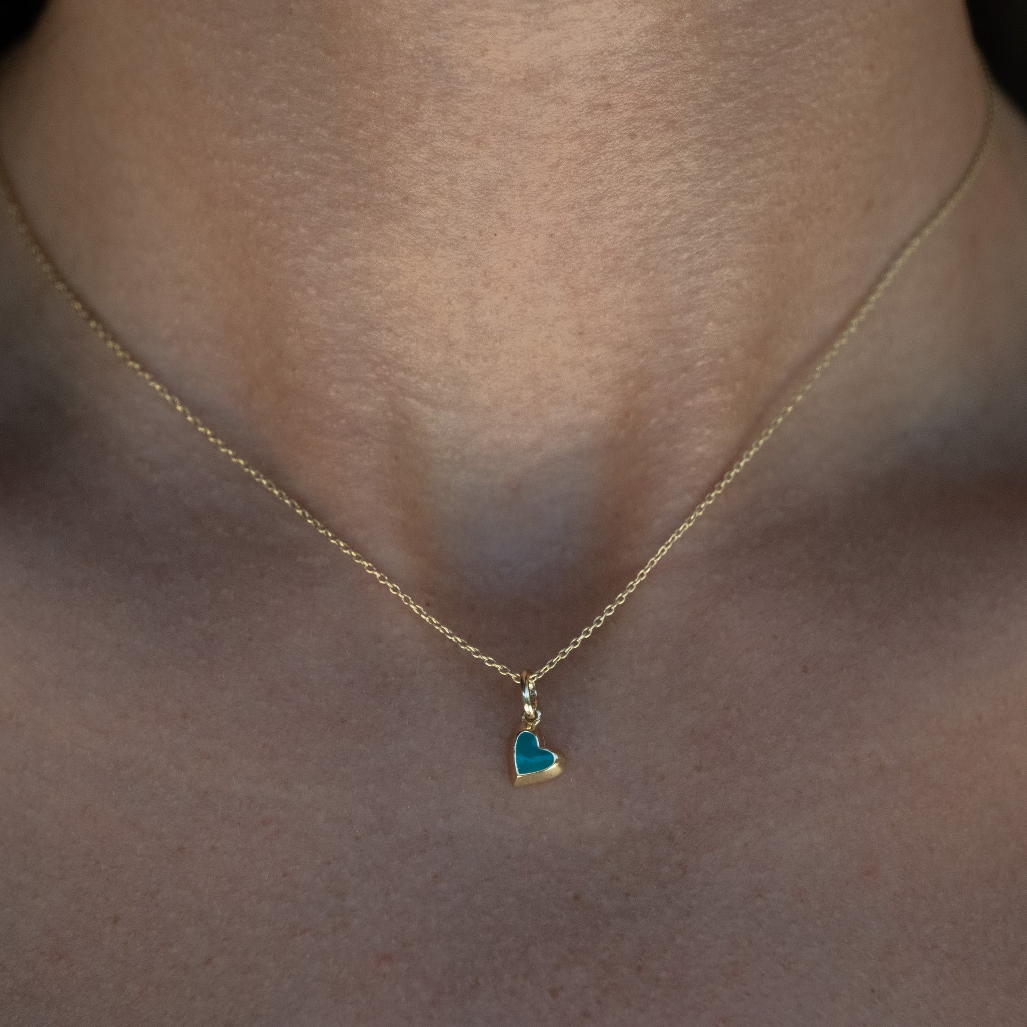 A woman wearing an Aiden Jae Mini Reversible Heart Charm Necklace with a blue heart on it.
