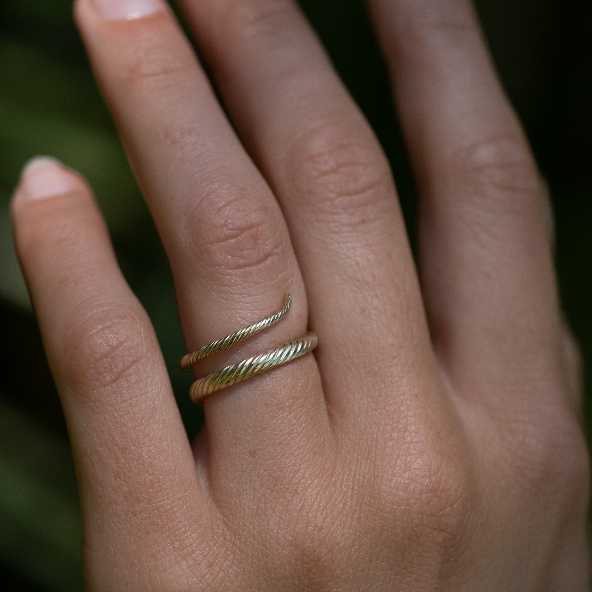 A model's hand wearing the Aiden Jae Banyan Wrap Ring in yellow gold with twisted texture..