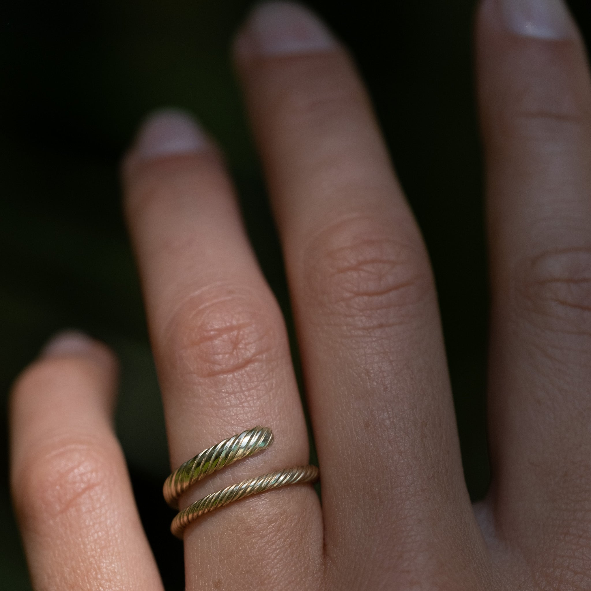 A model's hand wearing the Aiden Jae Banyan Wrap Ring in yellow gold with twisted texture..