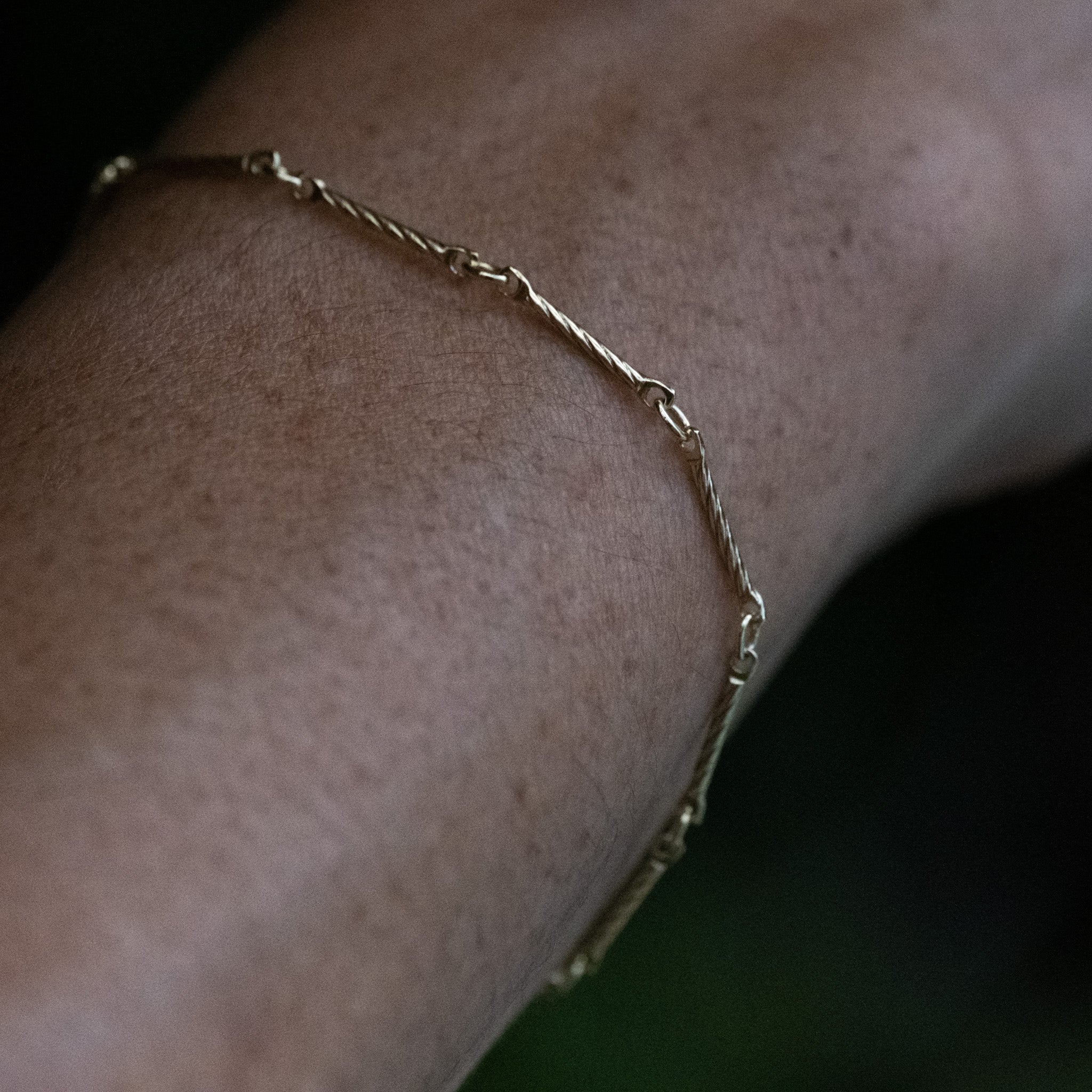 Close-up of solid gold bar chain bracelet with twisted texture, worn on wrist.