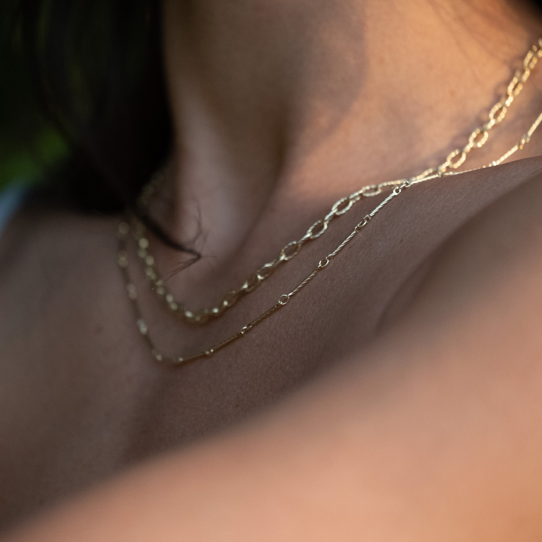 Minimalist solid gold bar chain necklace with twisted texture, worn on neck layered with another gold chain.