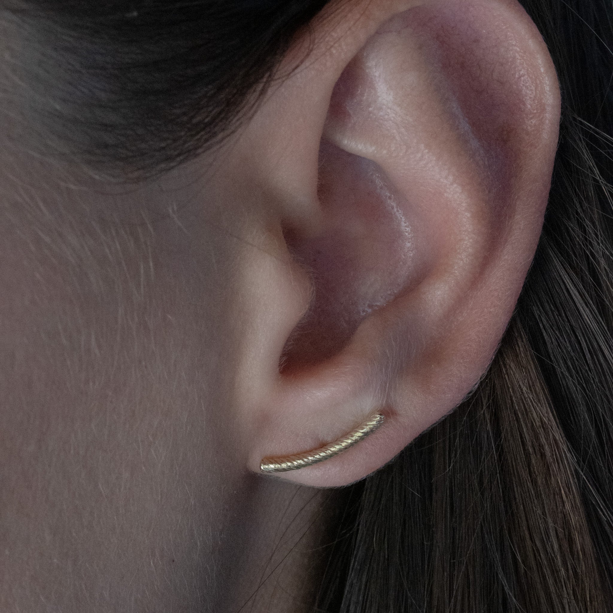 Solid gold bar stud earring with twisted texture and curved minimalist design, worn on ear.