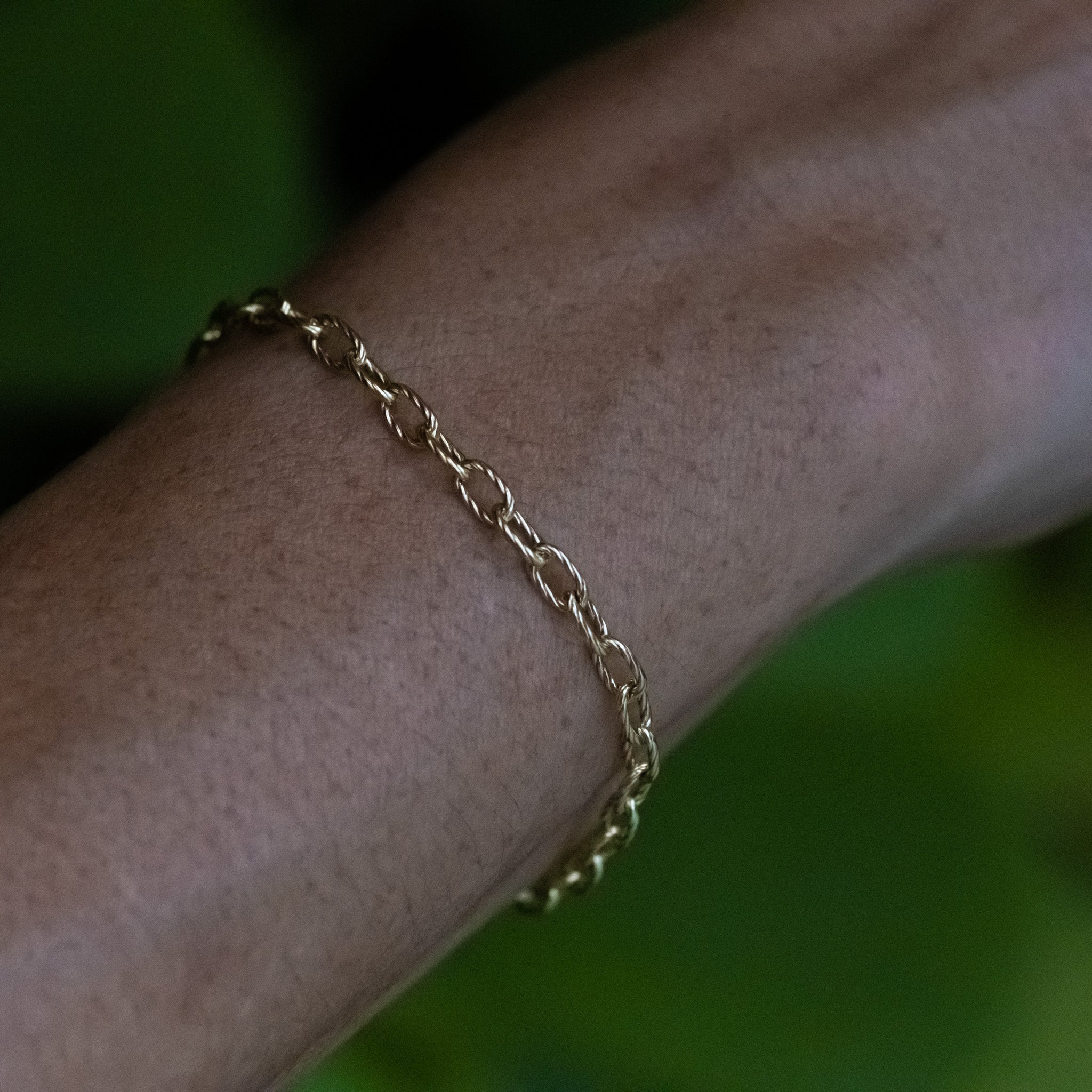 Solid gold cable chain bracelet with twisted texture worn on wrist, showing bold oval links.