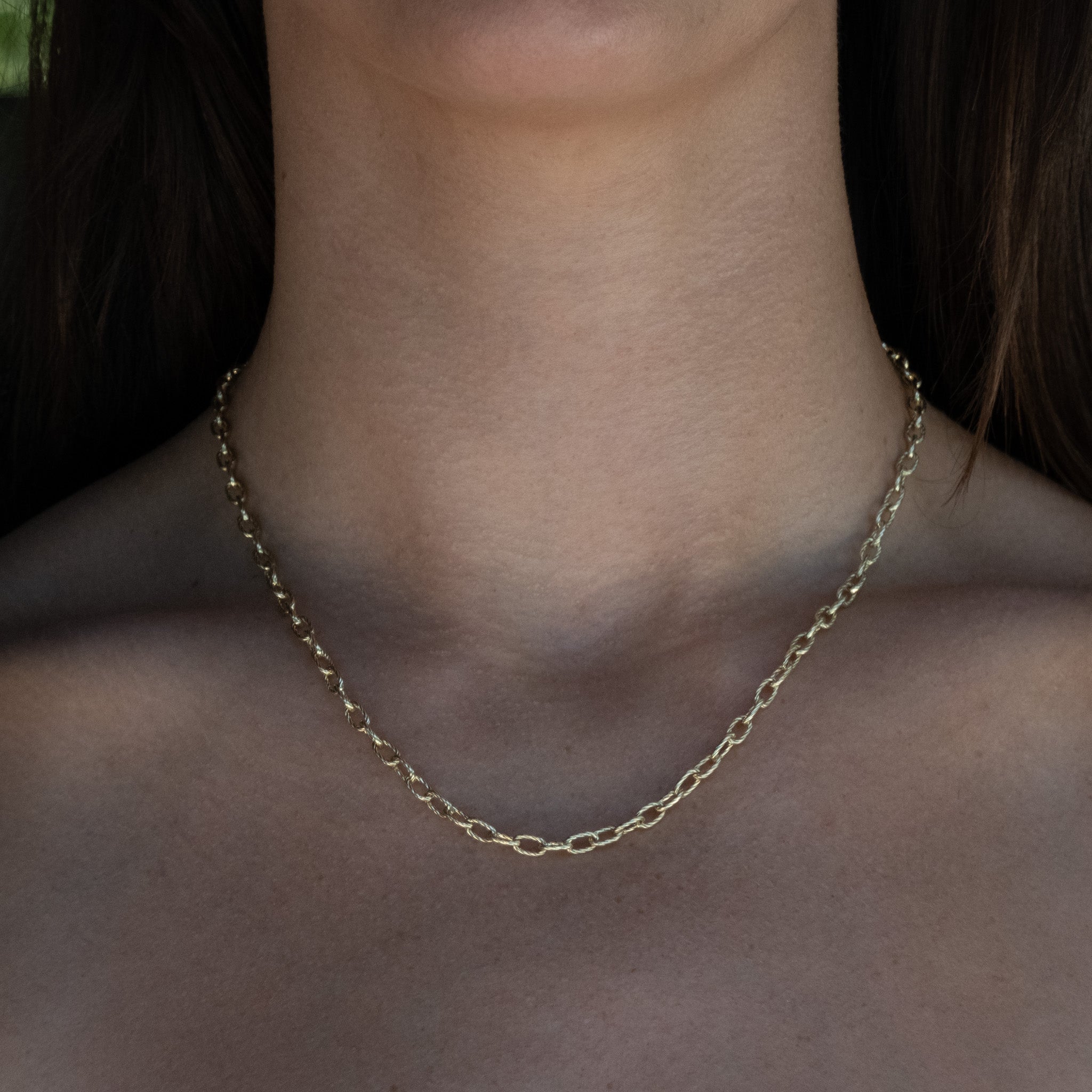 Solid gold cable chain necklace with twisted texture and bold oval links, worn on neck.