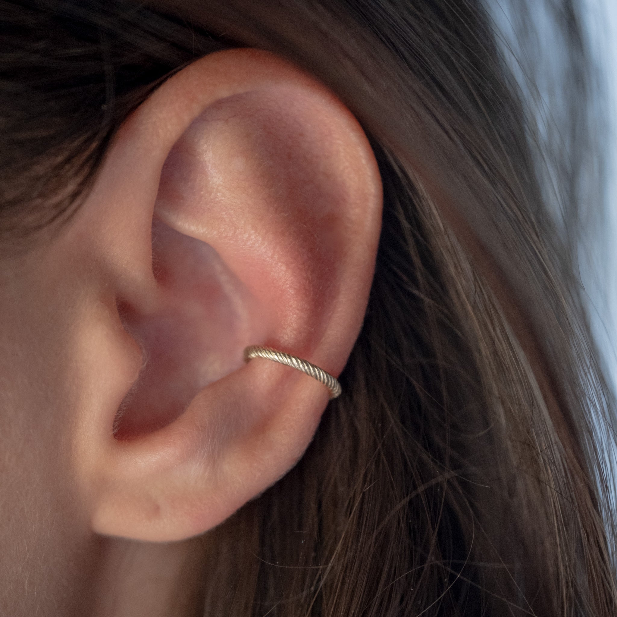Solid gold ear cuff with twisted texture and minimalist design, worn mid-ear.