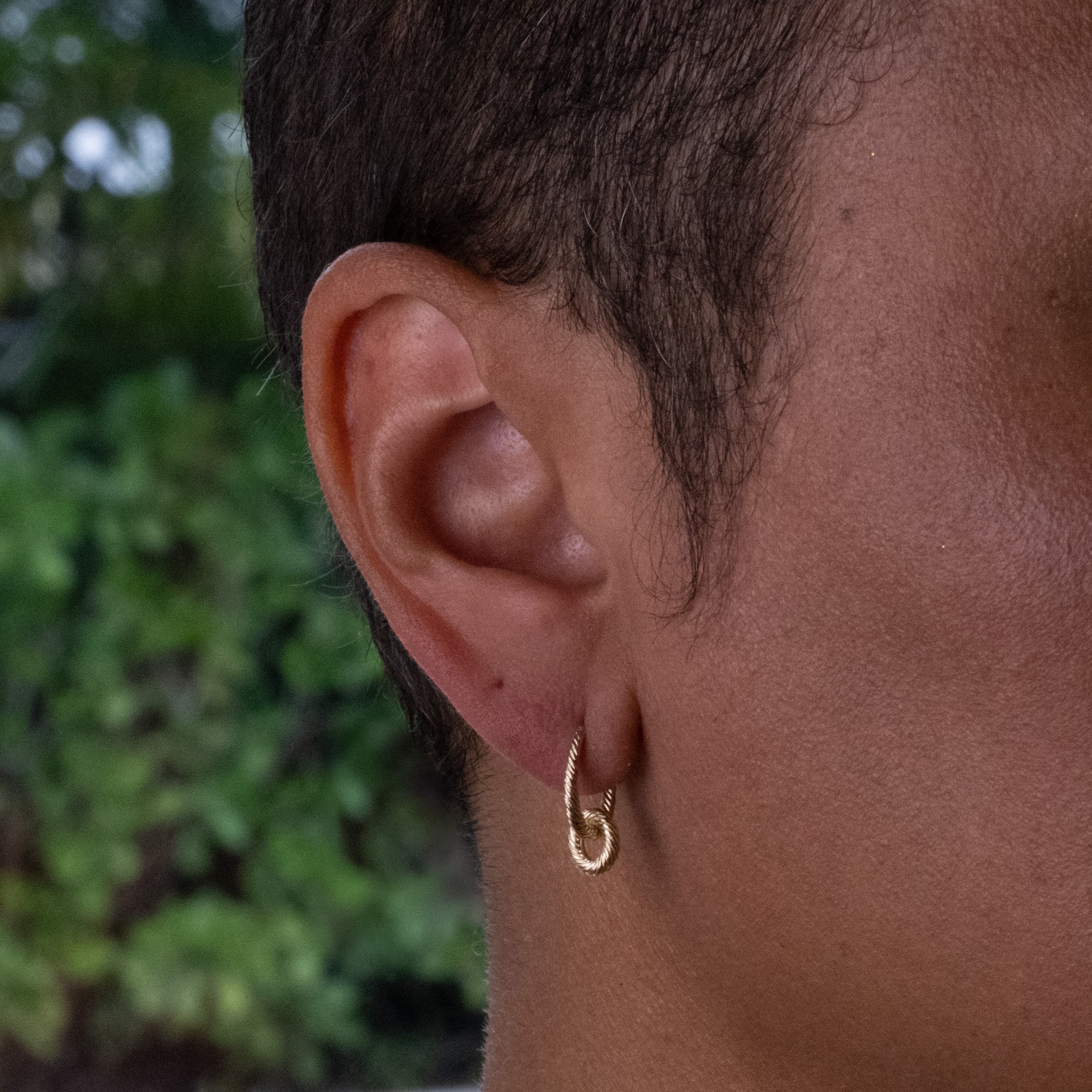 Solid gold hoop earring with removable link charm and twisted texture, worn on ear.